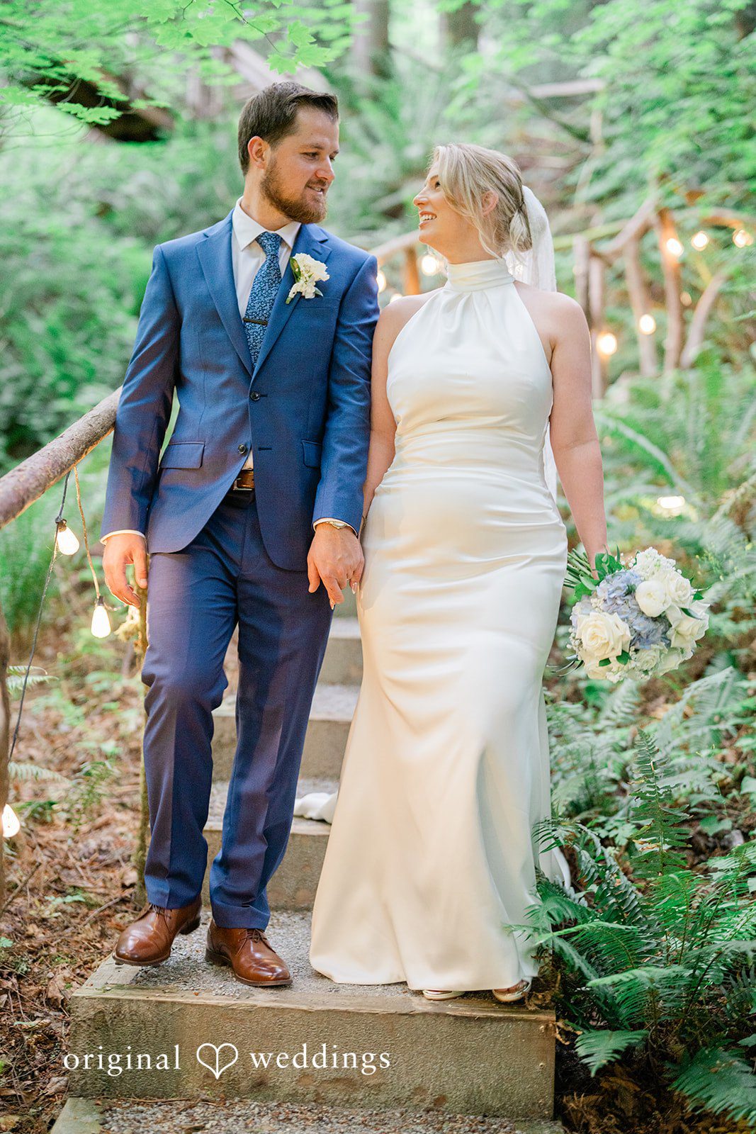 Destiny + Maksim A bride and groom walking hand-in-hand through a wooded area.