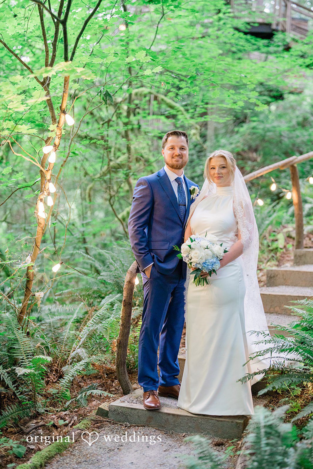Destiny + Maksim A bride and groom posing together on a stone staircase decorated with lights.