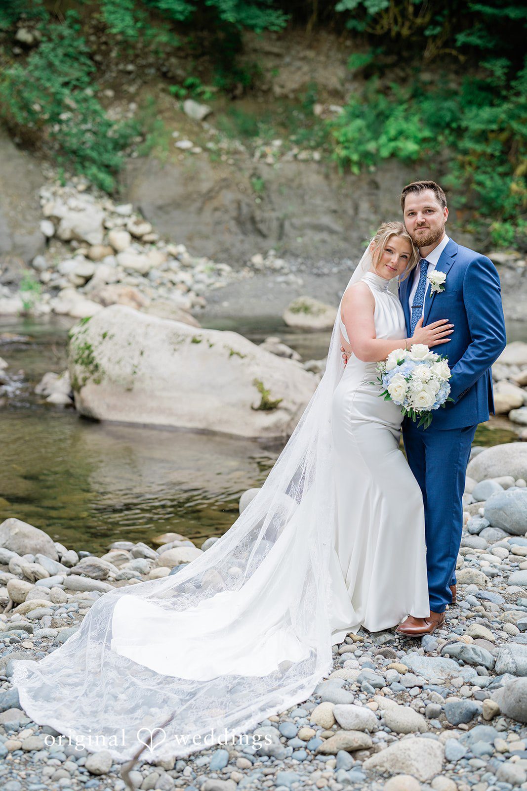 Destiny + Maksim A groom looking down lovingly at his bride who is resting on a rock by a stream.