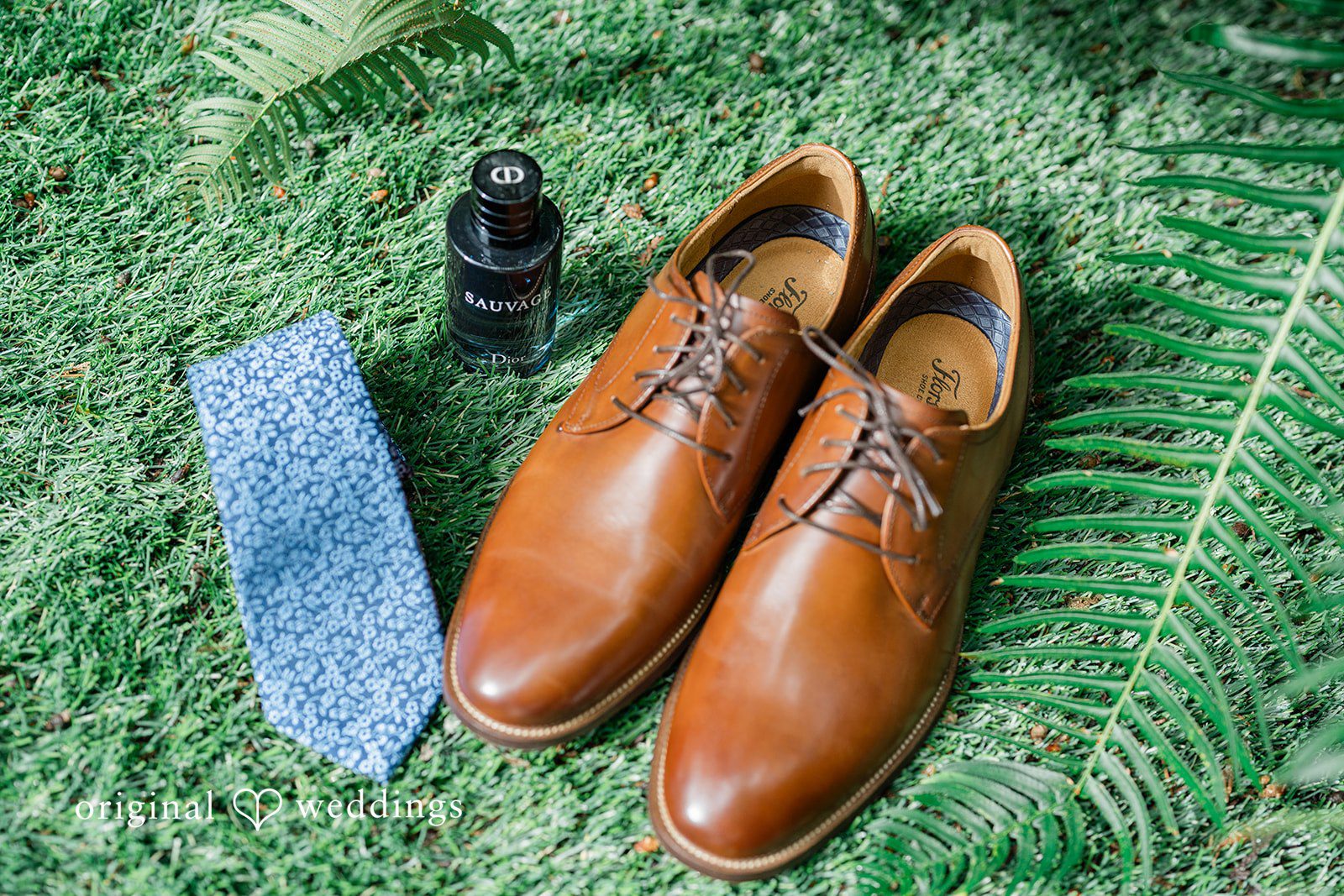 Destiny + Maksim A groom's flat lay featuring brown leather shoes, a blue tie, and a boutonnière.