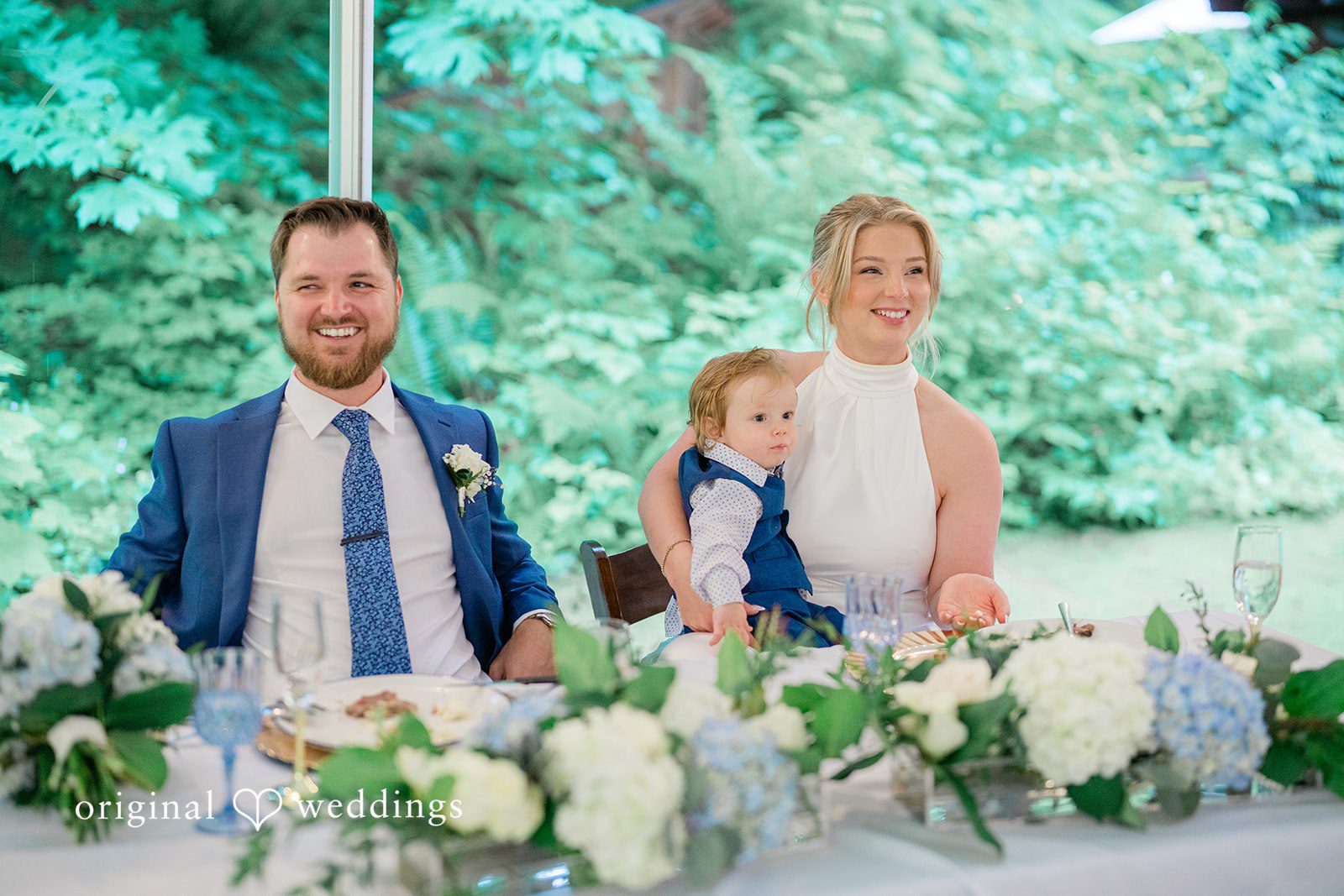 Destiny + Maksim A bride and groom sitting at their head table with a young child.
