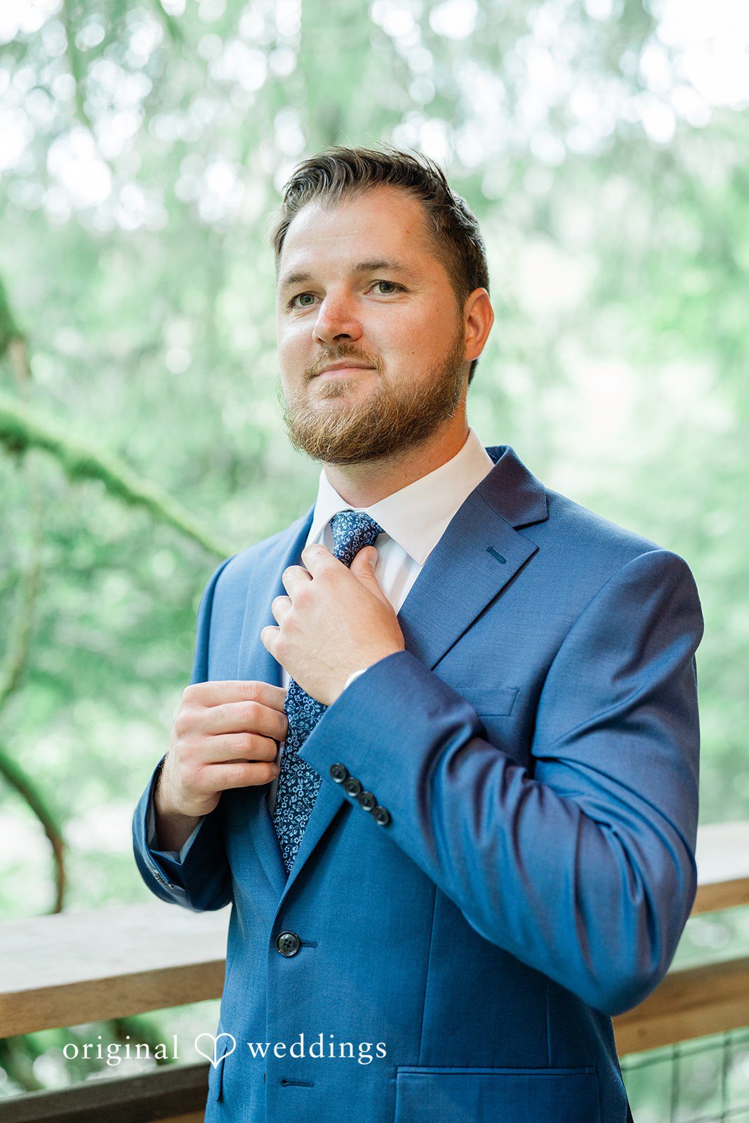 Destiny + Maksim A groom adjusting his tie while wearing a blue suit.