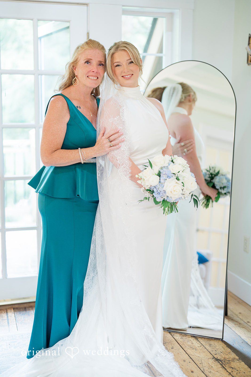 Destiny + Maksim A smiling bride posing with a woman in a teal dress in front of a mirror.