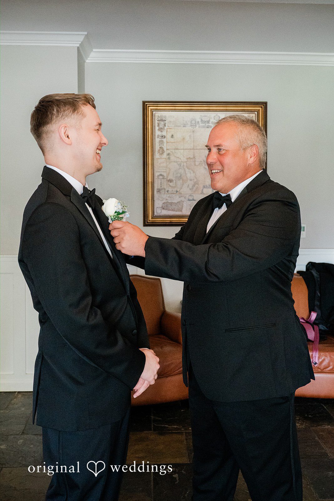 Luke + Kelsey Two men in black suits adjusting a lapel and smiling at each other.