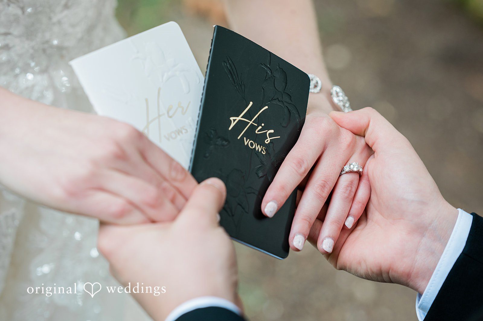 Luke + Kelsey Close-up of a groom holding a black vow book while a bride places a ring on his finger.
