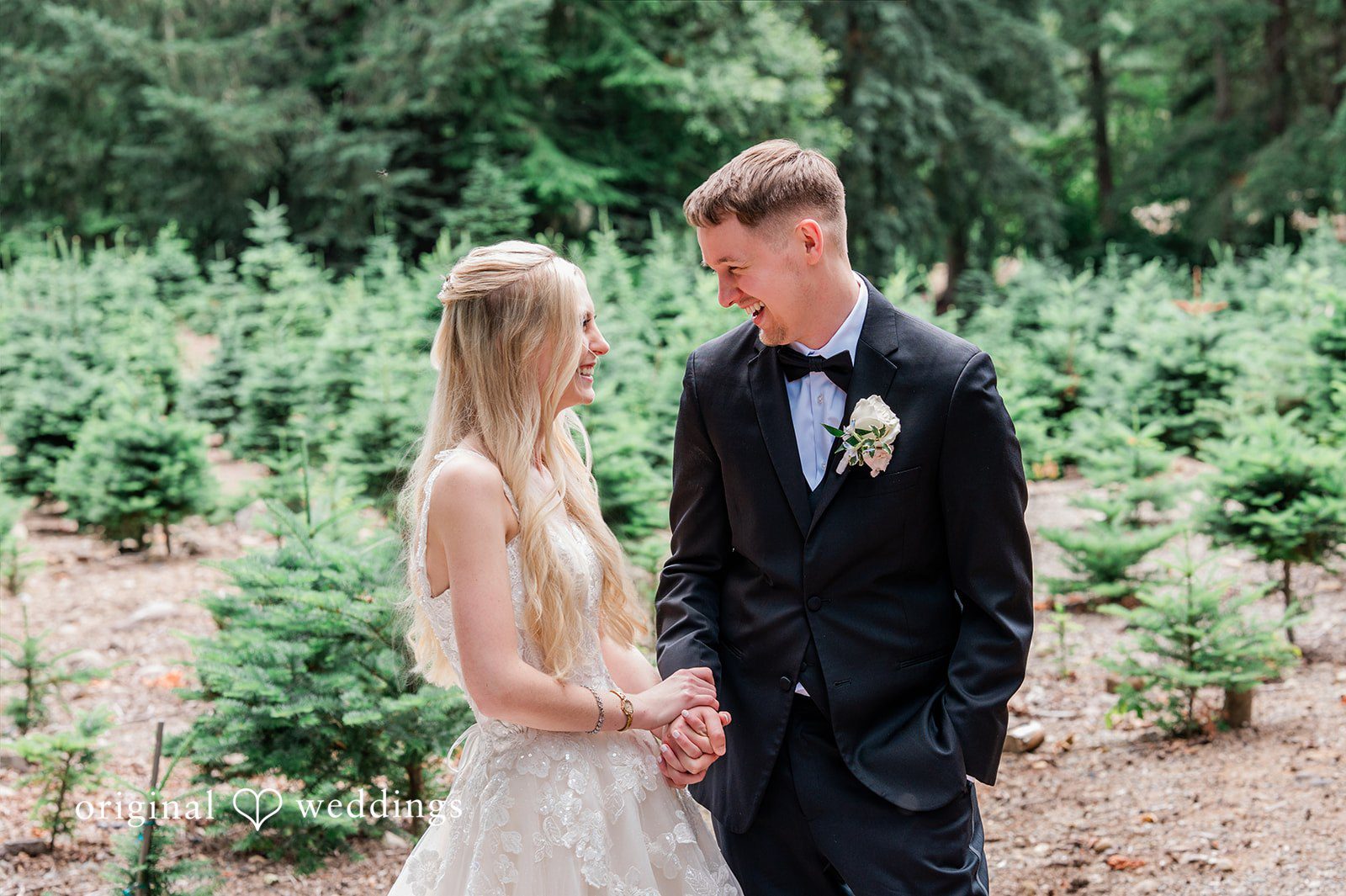 Luke + Kelsey A bride and groom holding hands while looking at each other in a field.