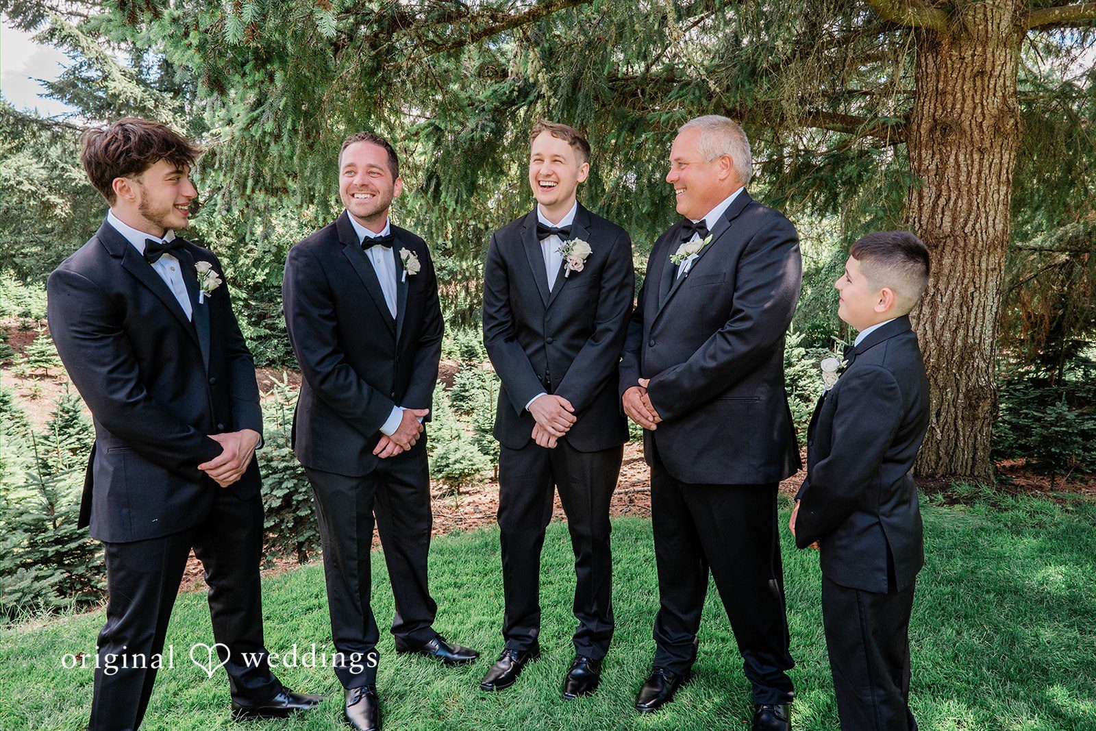 Luke + Kelsey Grooms and groomsmen in dark suits standing together in a line outside.