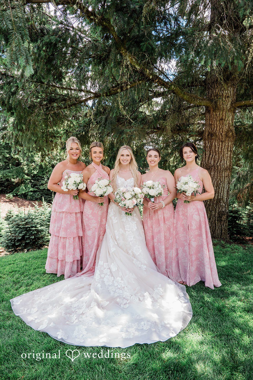 Luke + Kelsey A bride standing with four bridesmaids wearing long pink dresses on a lawn.