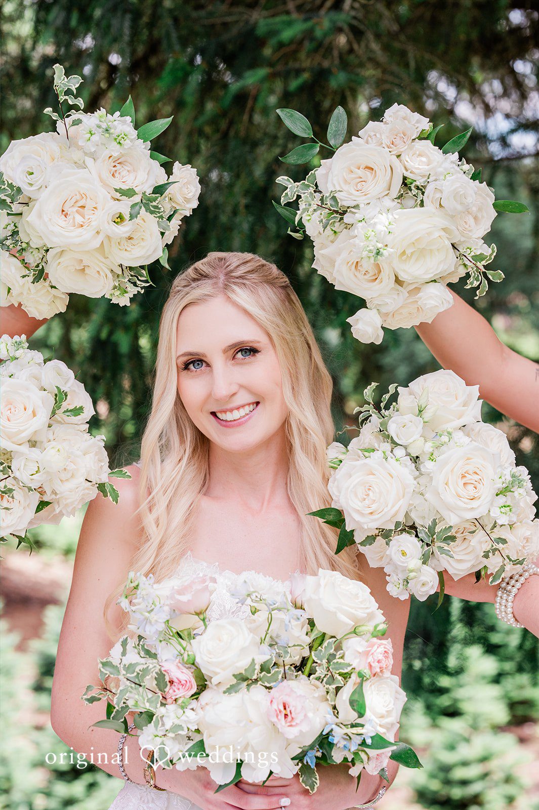 Luke + Kelsey A bride smiling while holding her bouquet surrounded by white flowers.