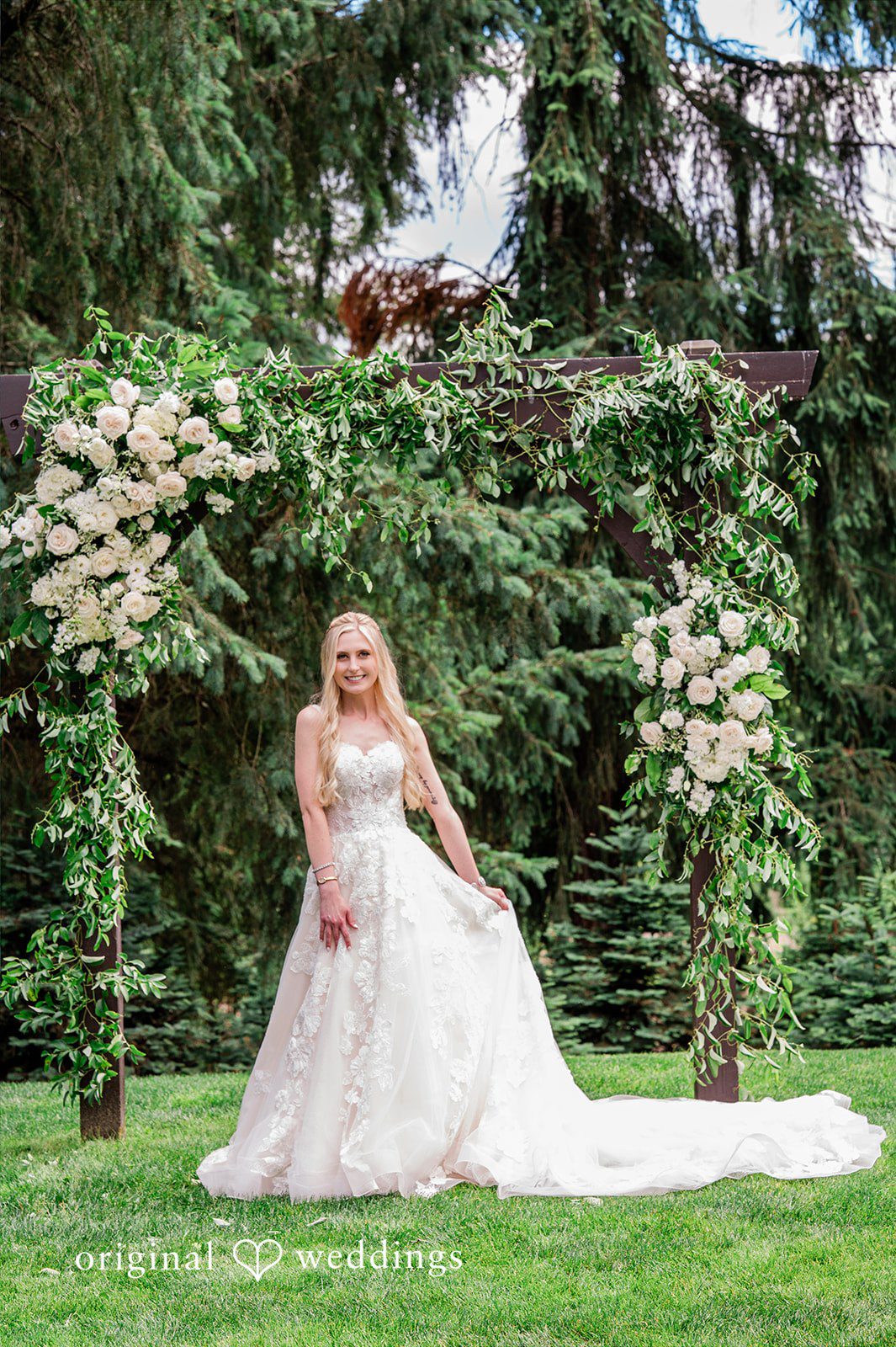 Luke + Kelsey A bride in her wedding dress on a grassy lawn with a greenery backdrop.