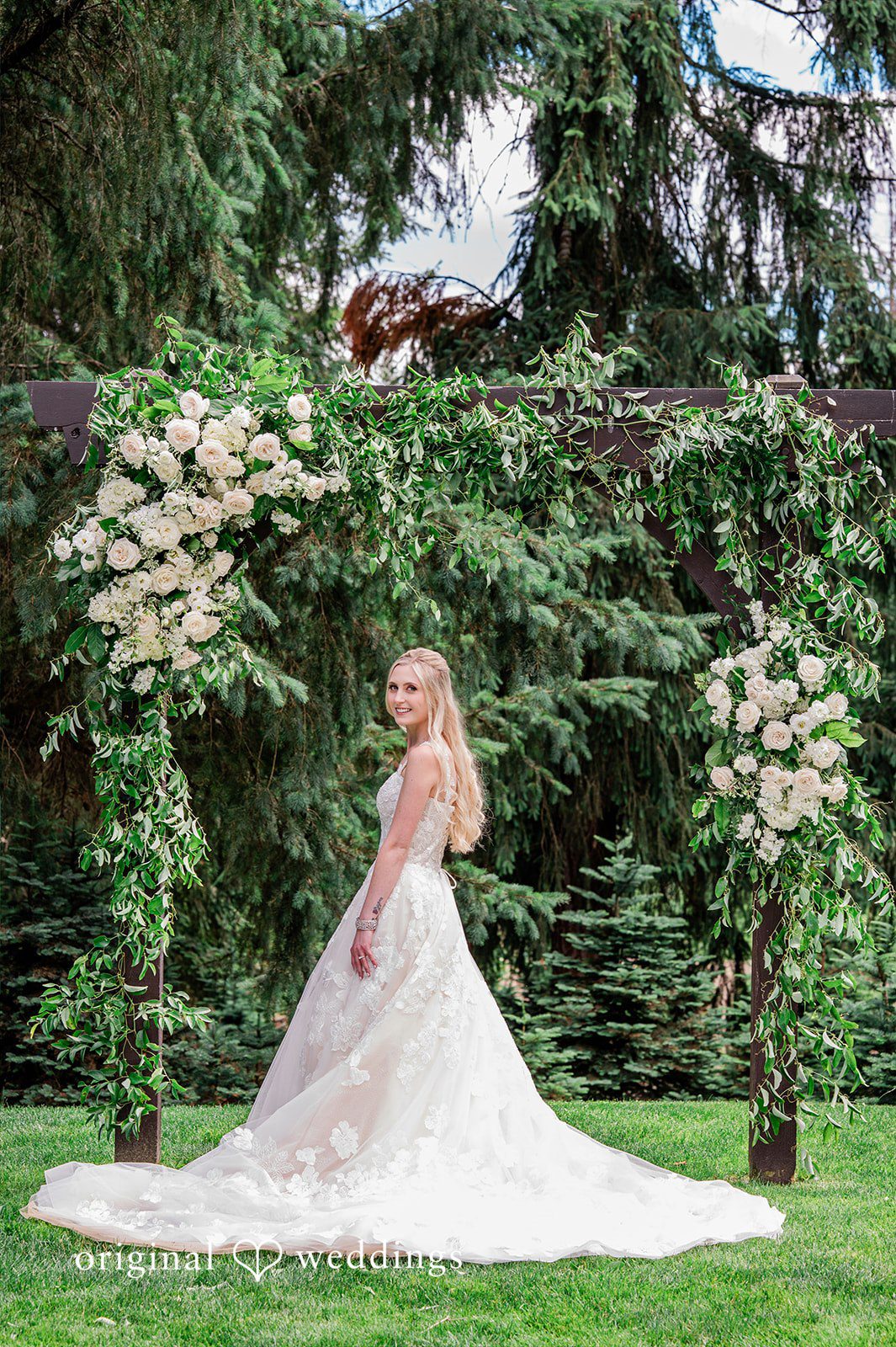 Luke + Kelsey A bride standing in her gown looking toward a scenic forest backdrop.