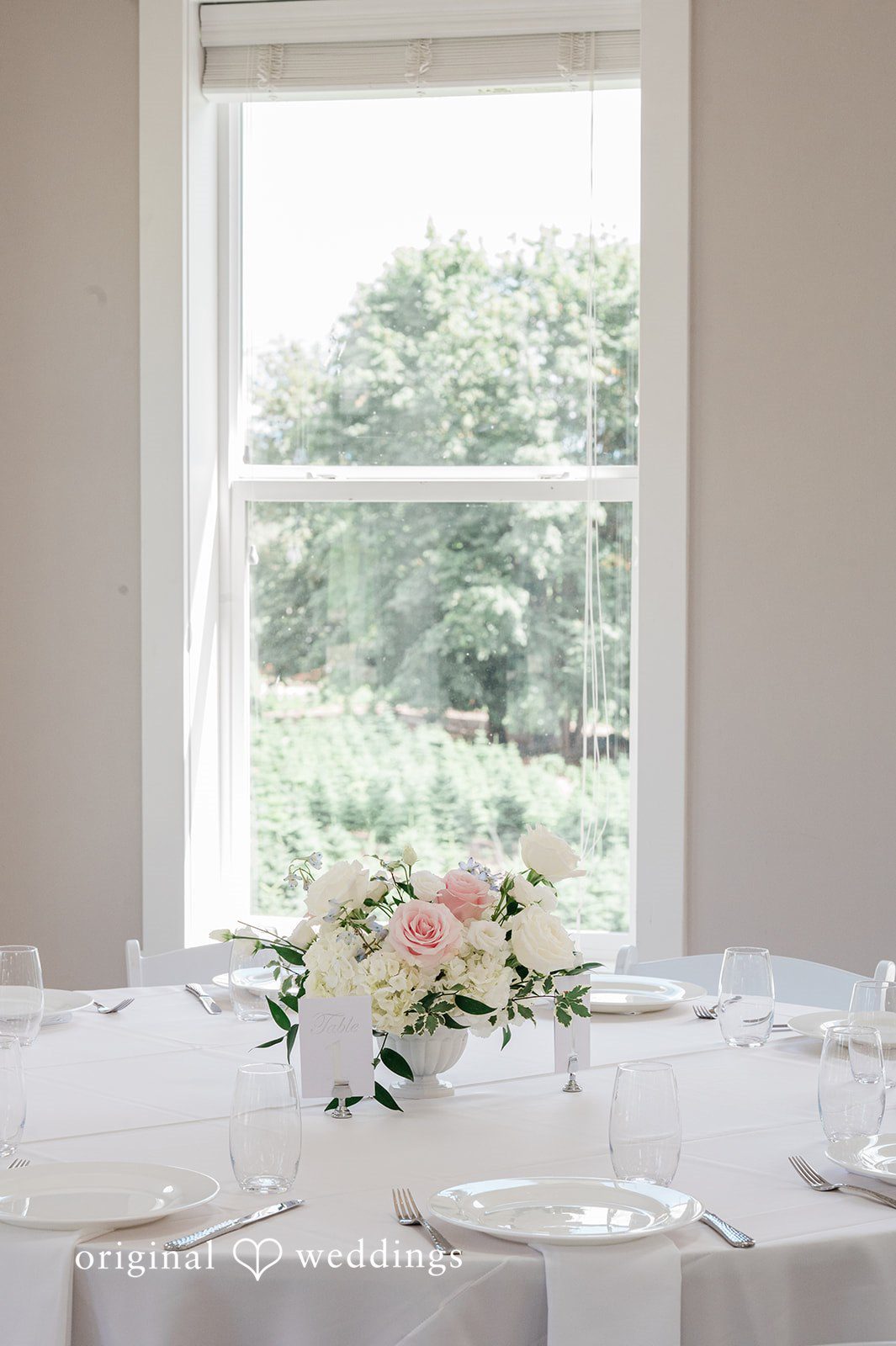 Luke + Kelsey A decorated reception table with floral arrangements positioned near a large window.