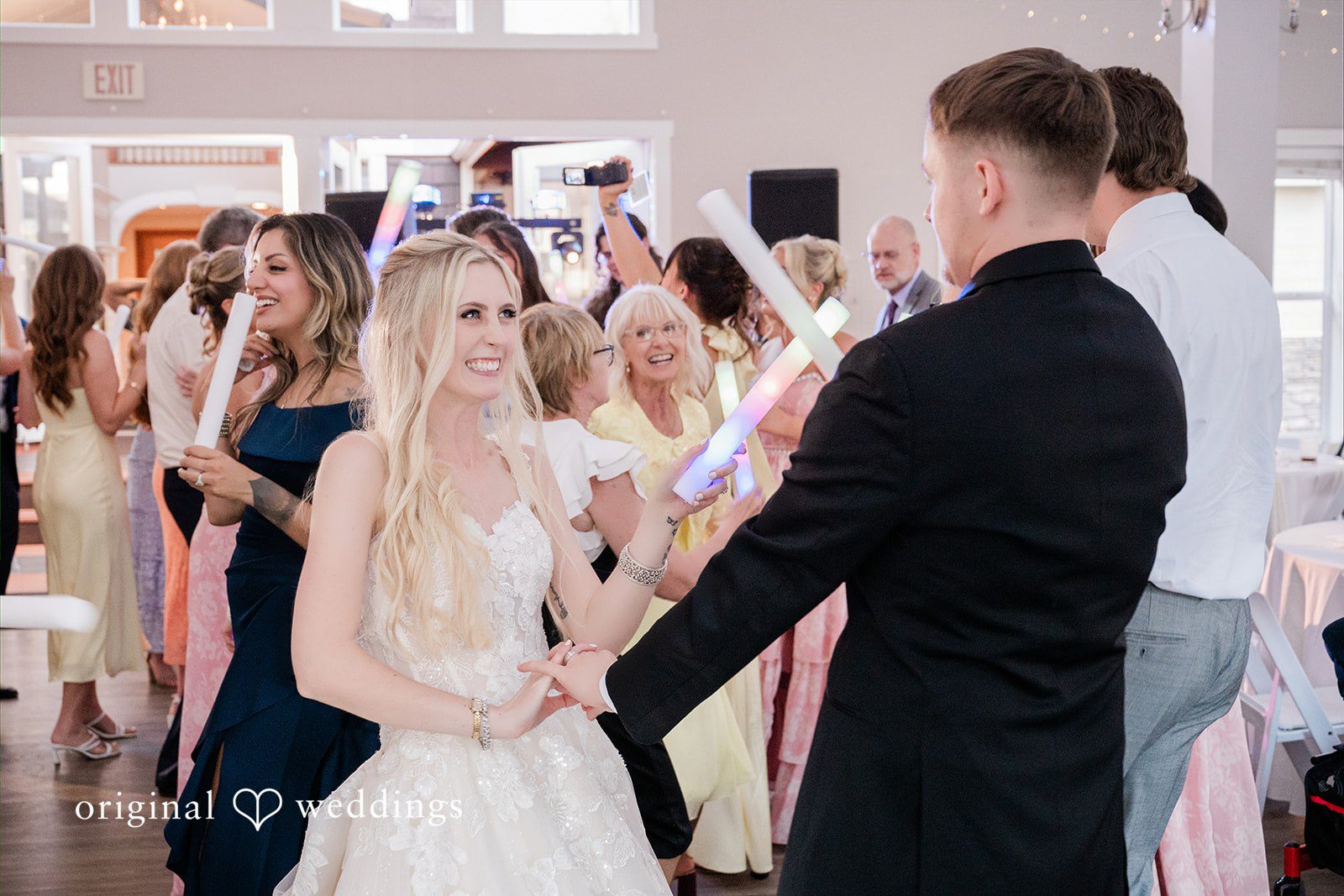Luke + Kelsey A bride and groom smiling at each other on a crowded dance floor.