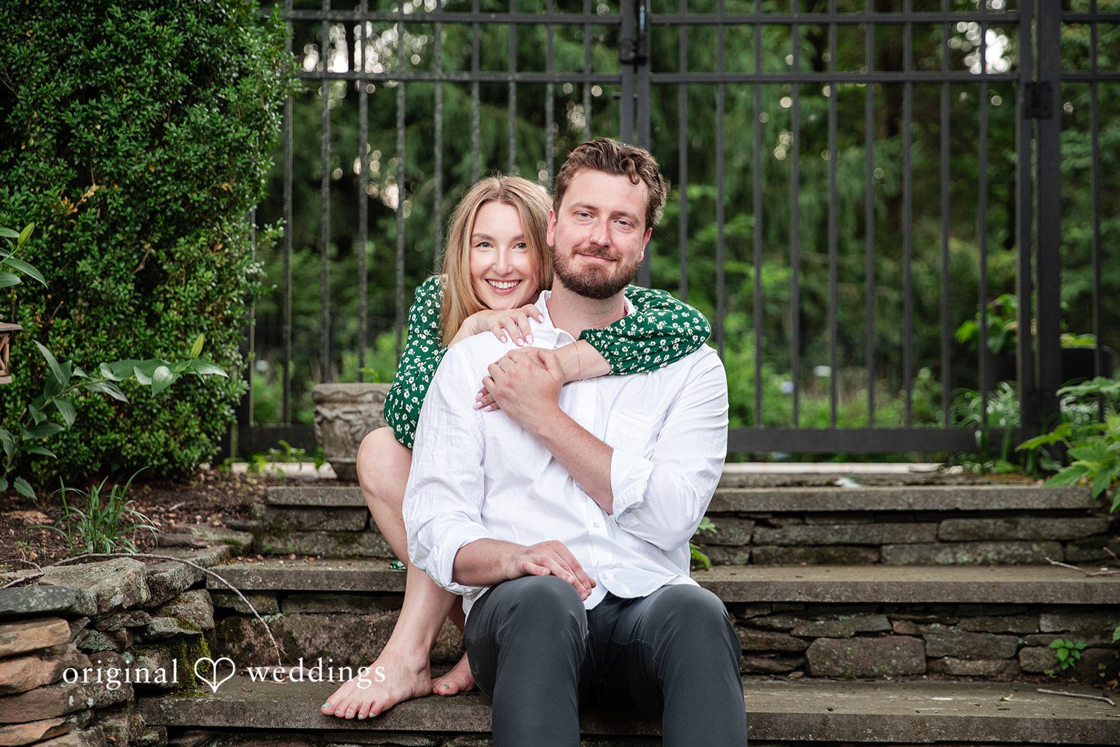 Sarah + Tyler A man sits on stone stairs while a woman sits comfortably in his lap smiling.