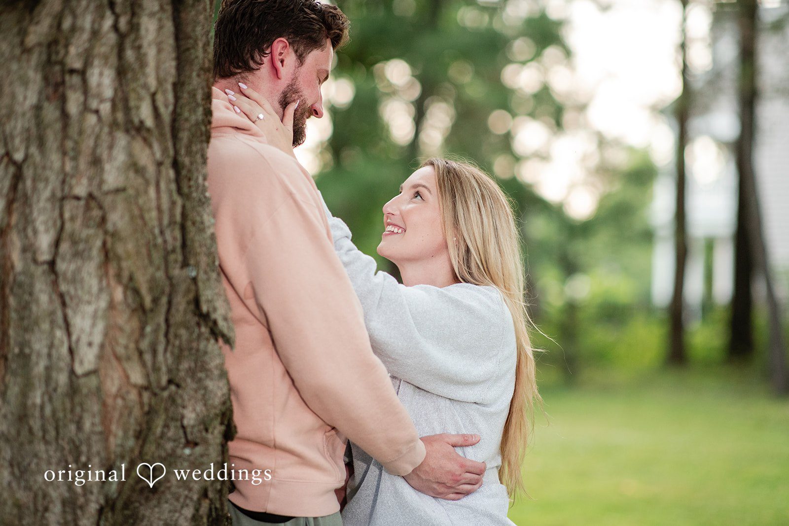 Sarah + Tyler A man in a pink hoodie hugs a woman in a white sweater while looking into her eyes.