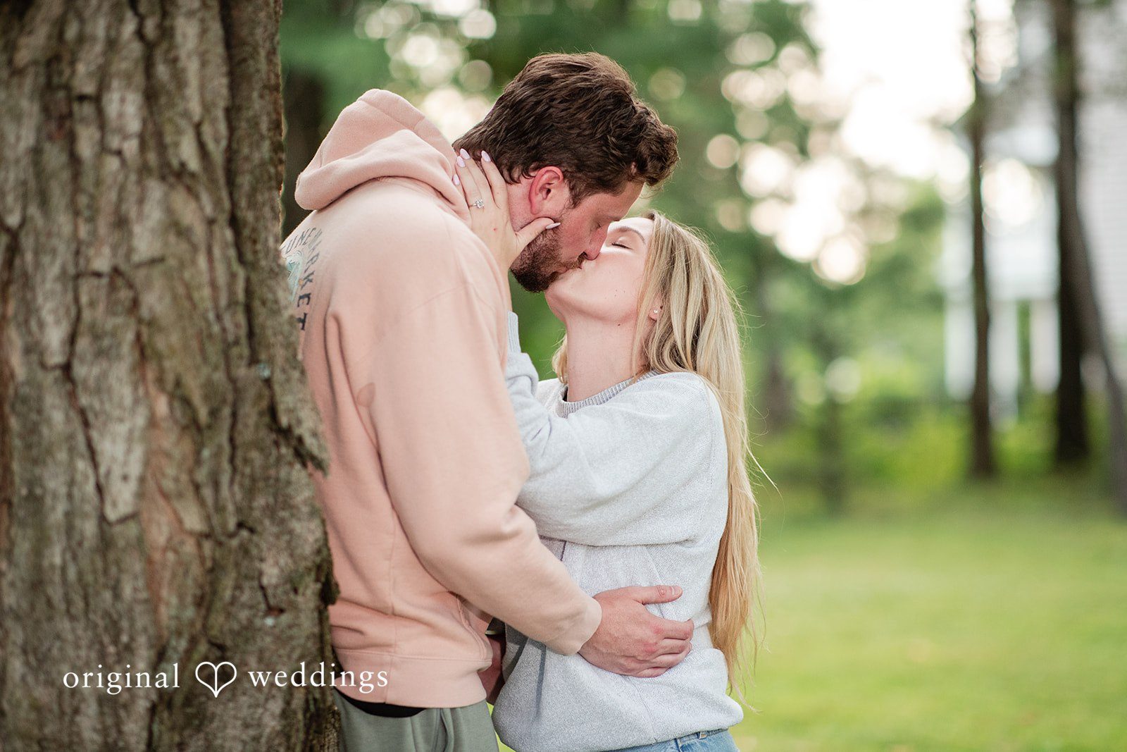 Sarah + Tyler A man in a pink hoodie hugs a woman in a white sweater while looking into her eyes.