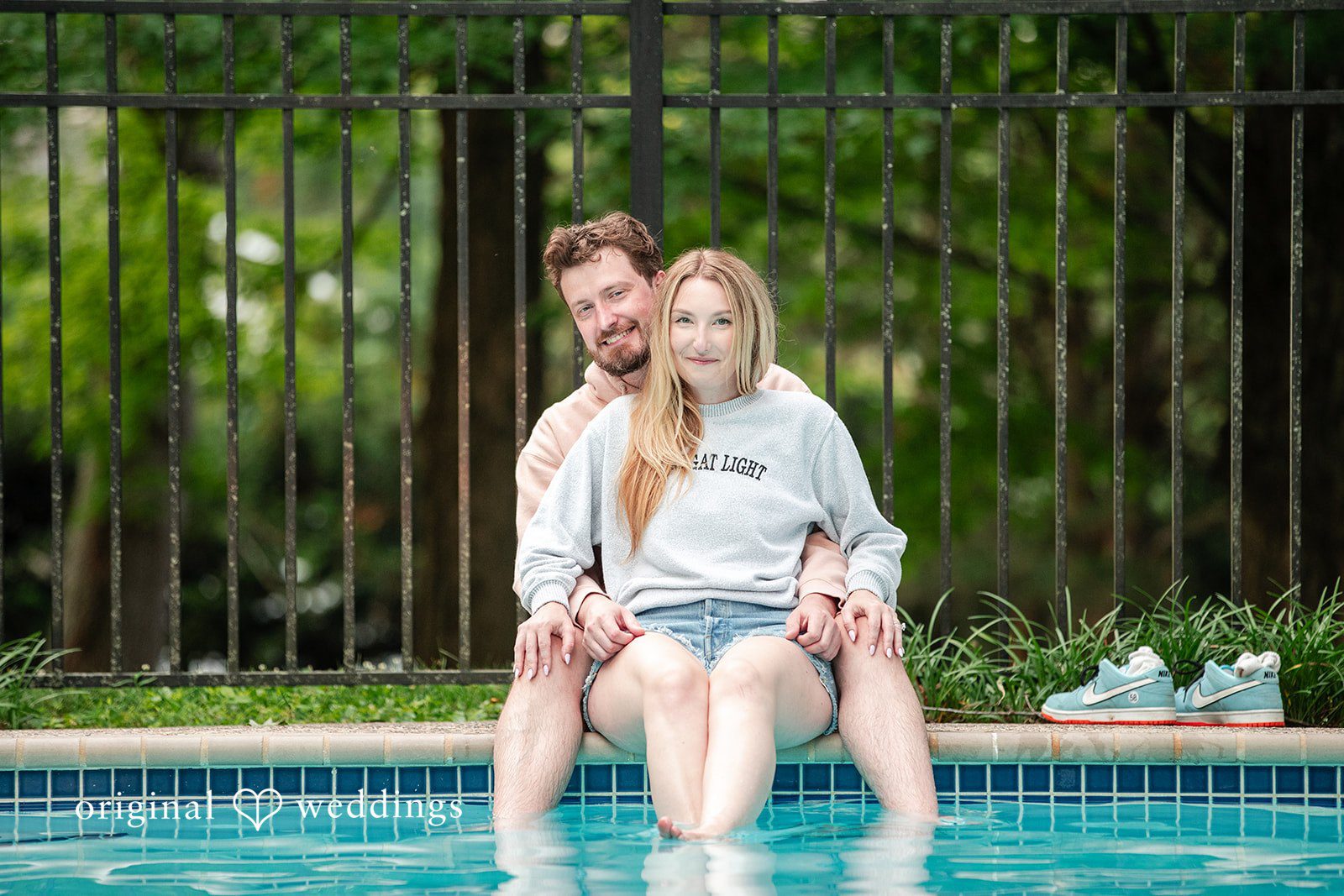 Sarah + Tyler A woman sits on a man's lap at the edge of a pool, both smiling.