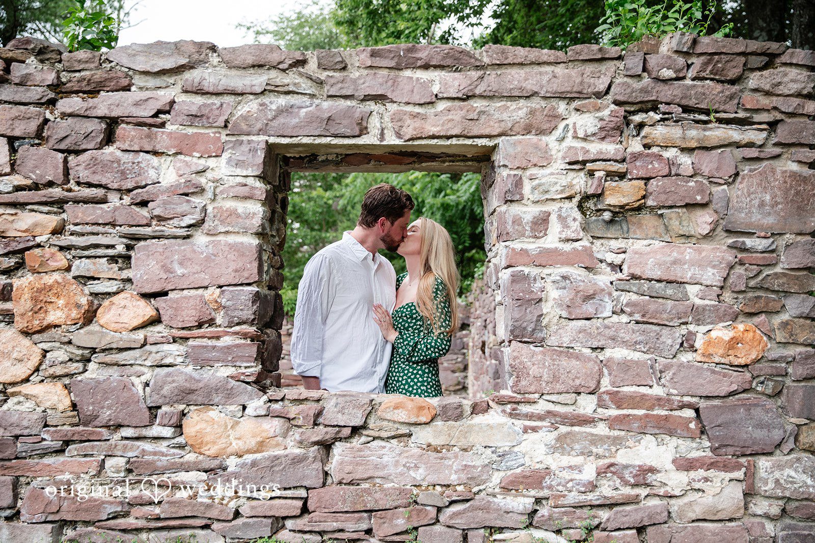 Sarah + Tyler A wide shot of a couple standing and embracing inside an old stone building's window opening.