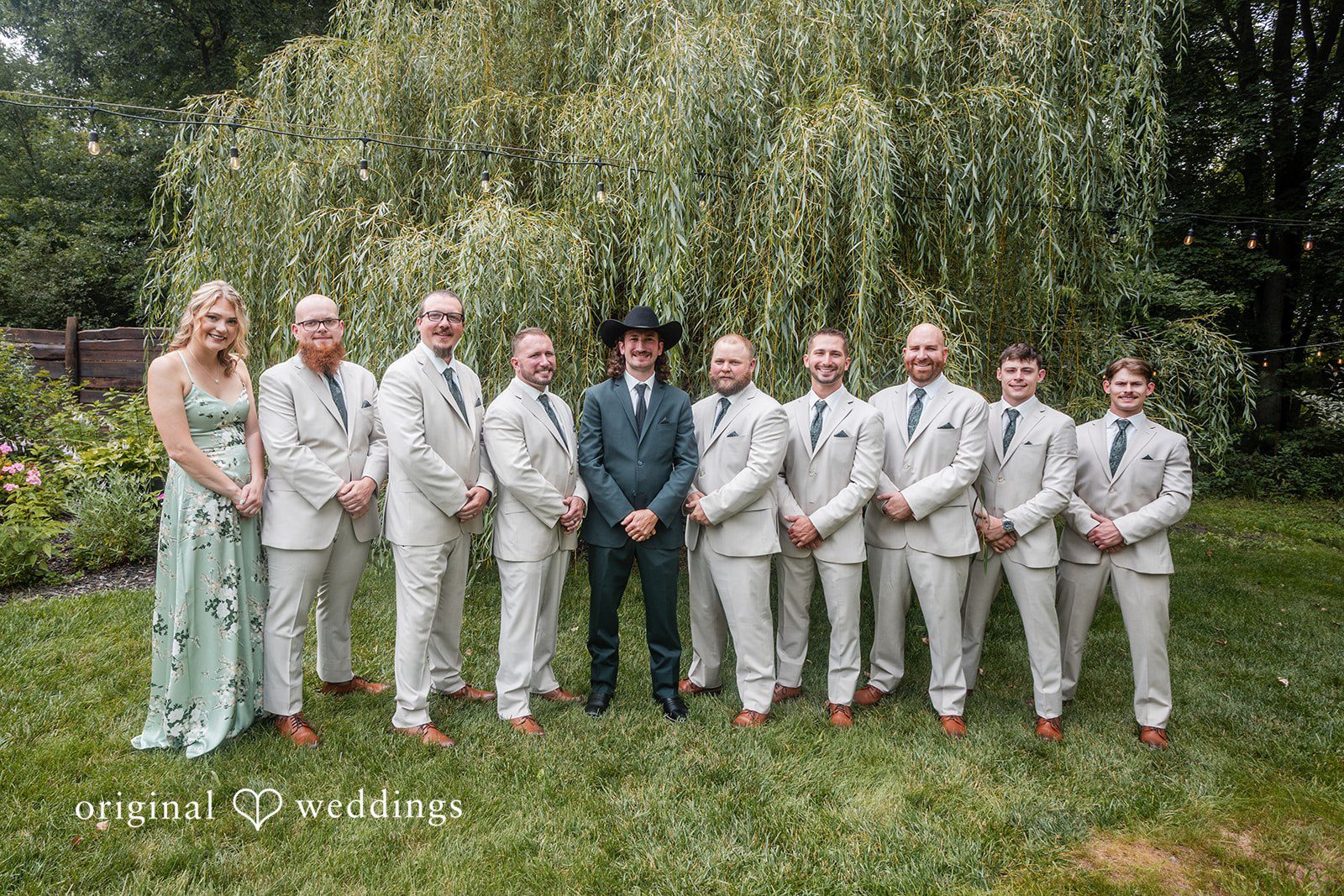 Savannah + Phillip A group of groomsmen wearing light gray suits and cowboy hats standing in a line on the grass.