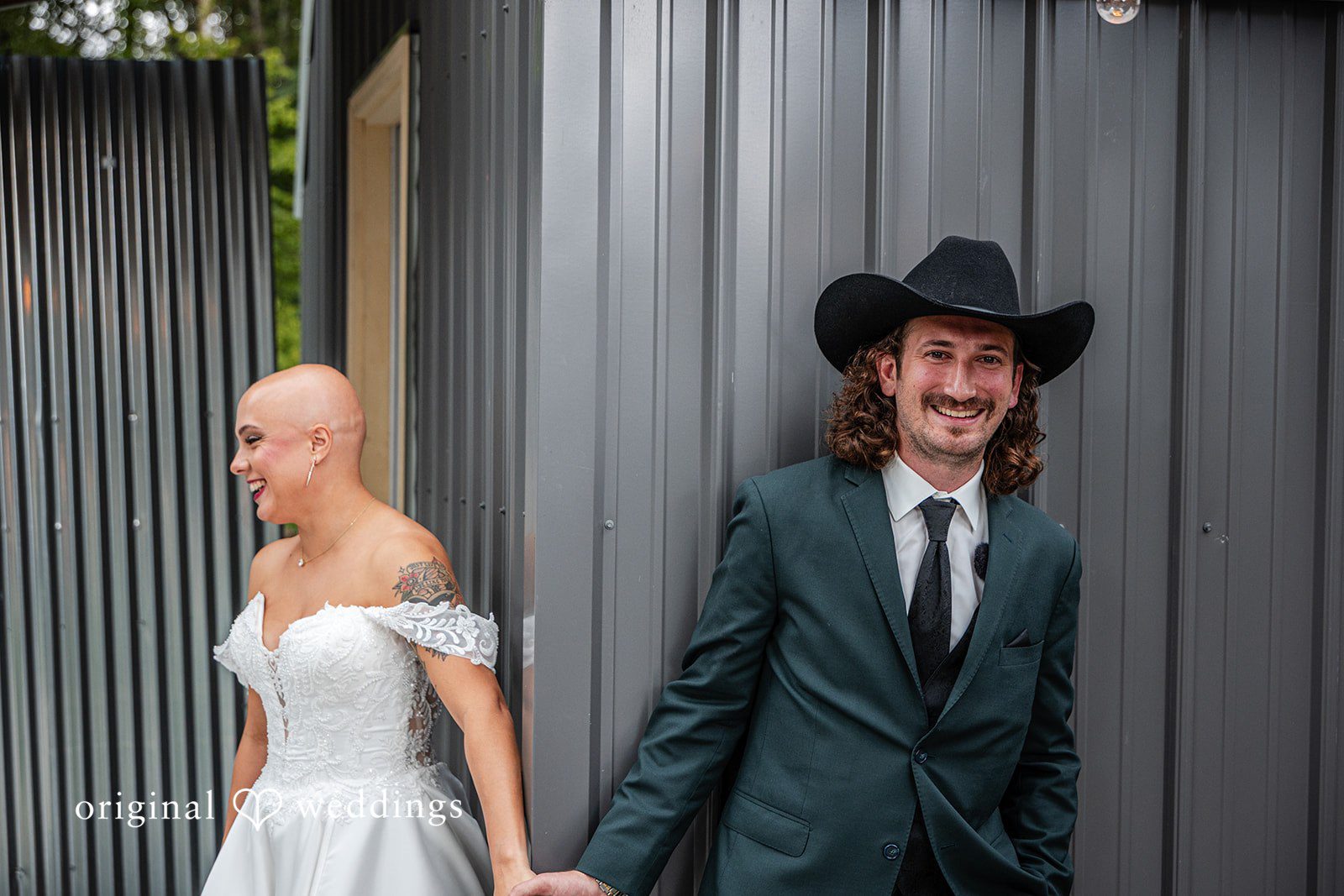 Savannah + Phillip A bride in a white gown and a groom in a dark suit walking together alongside a gray corrugated wall.