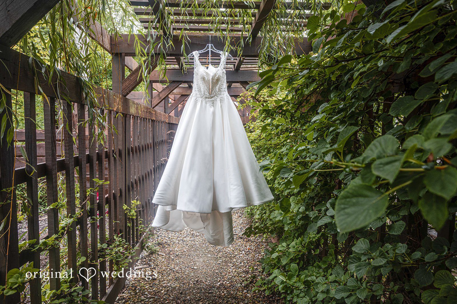 Savannah + Phillip A white wedding dress hanging up against a dark metal fence and green foliage.