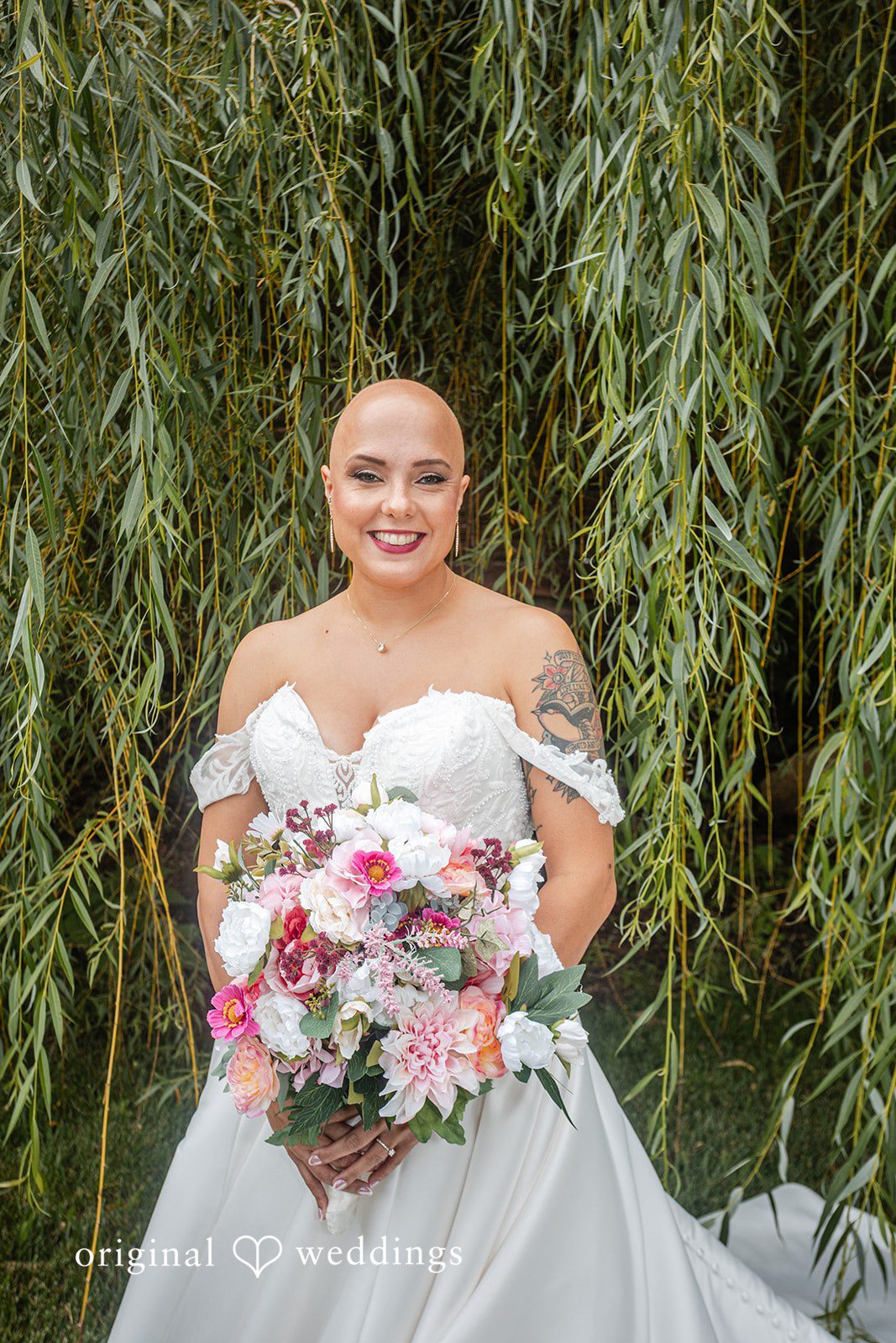Savannah + Phillip A smiling bride holding her bouquet in front of a willow tree backdrop.