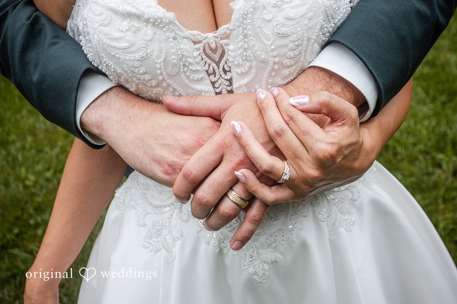 Savannah + Phillip A close-up shot of a bride and groom holding hands over the front of a white wedding dress.