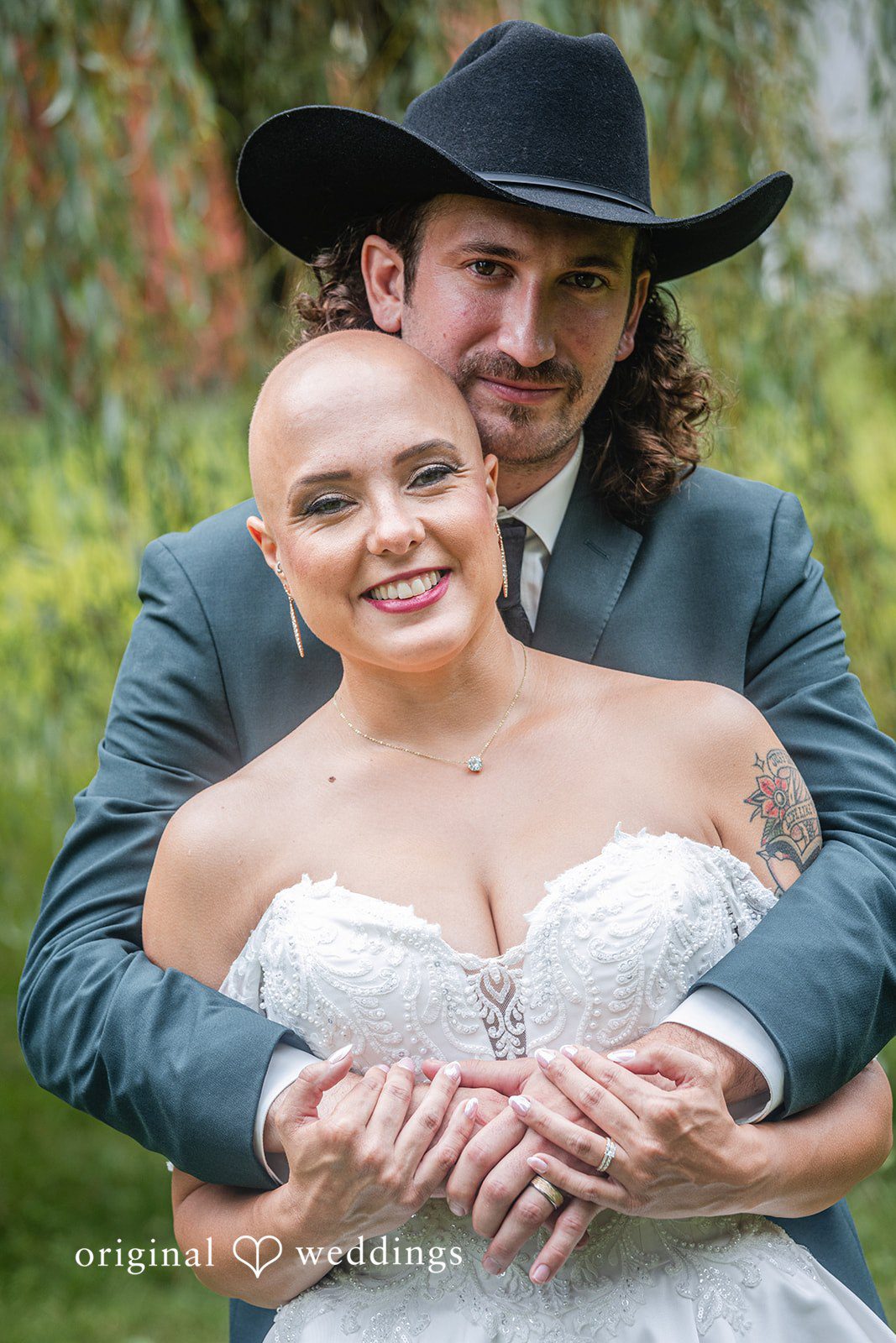Savannah + Phillip A groom in a cowboy hat hugging a smiling bride from behind while showing off their wedding rings.