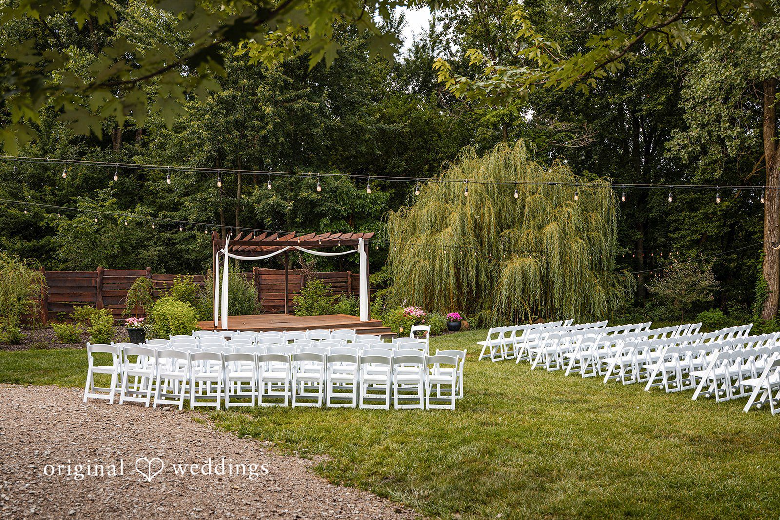 Savannah + Phillip Empty white chairs arranged for an outdoor wedding ceremony facing a wooden arbor.
