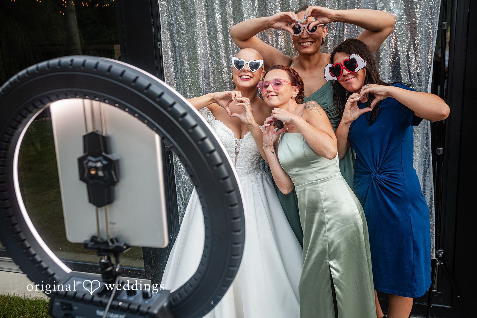 Savannah + Phillip A group of wedding guests posing with fun sunglasses in front of a photo booth ring light.