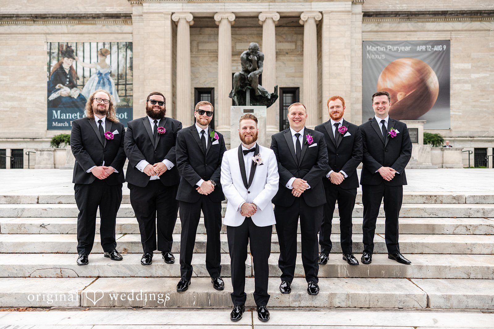 Dan + Alex A groom standing centrally in front of a line of groomsmen in matching black suits on stairs.