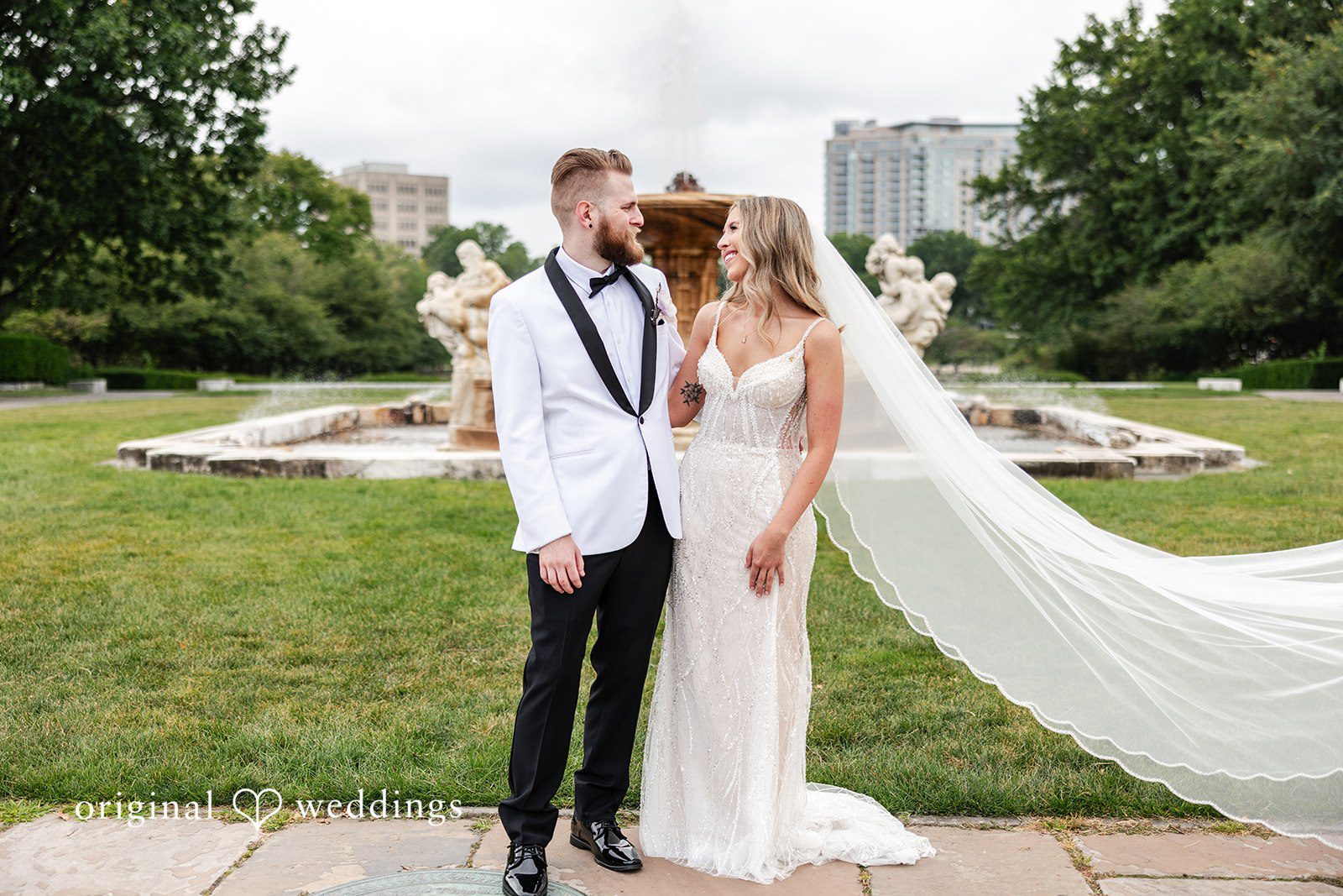 Dan + Alex A bride with a long flowing veil standing next to her groom on a lawn.