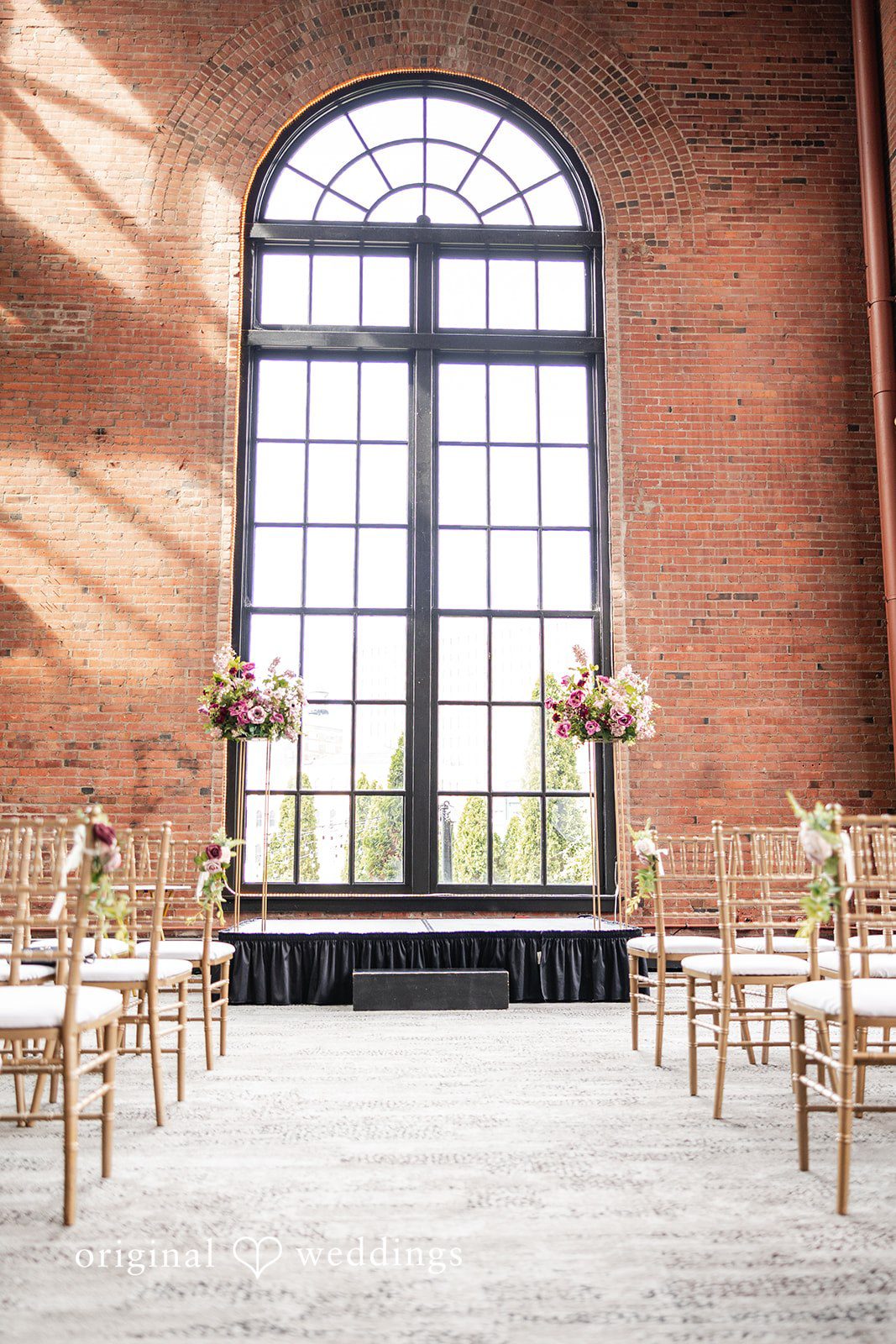 Dan + Alex A wedding ceremony setup with rows of empty wooden chairs facing large glass windows.