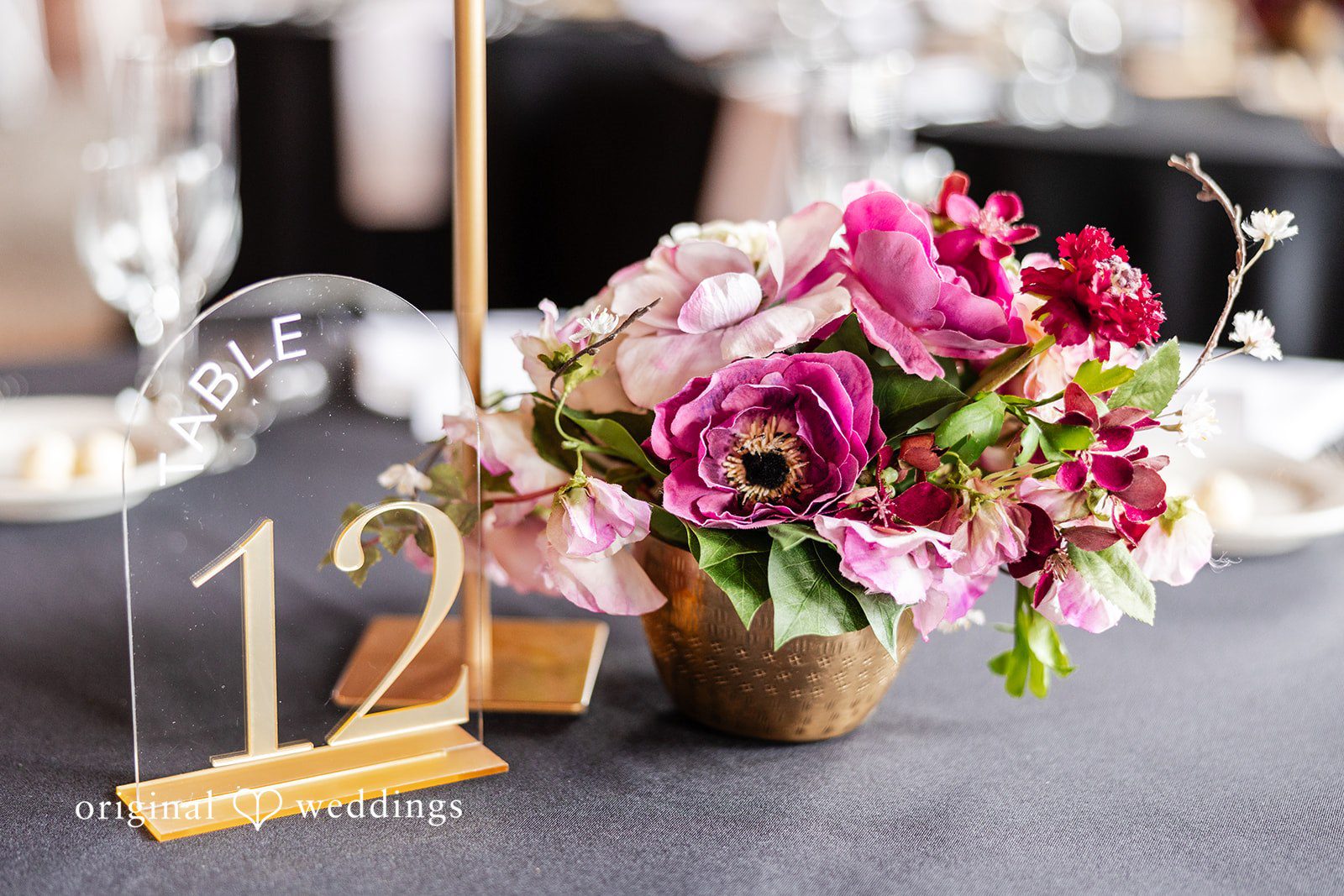 Dan + Alex A reception table center arrangement featuring vibrant pink flowers next to a gold table number.
