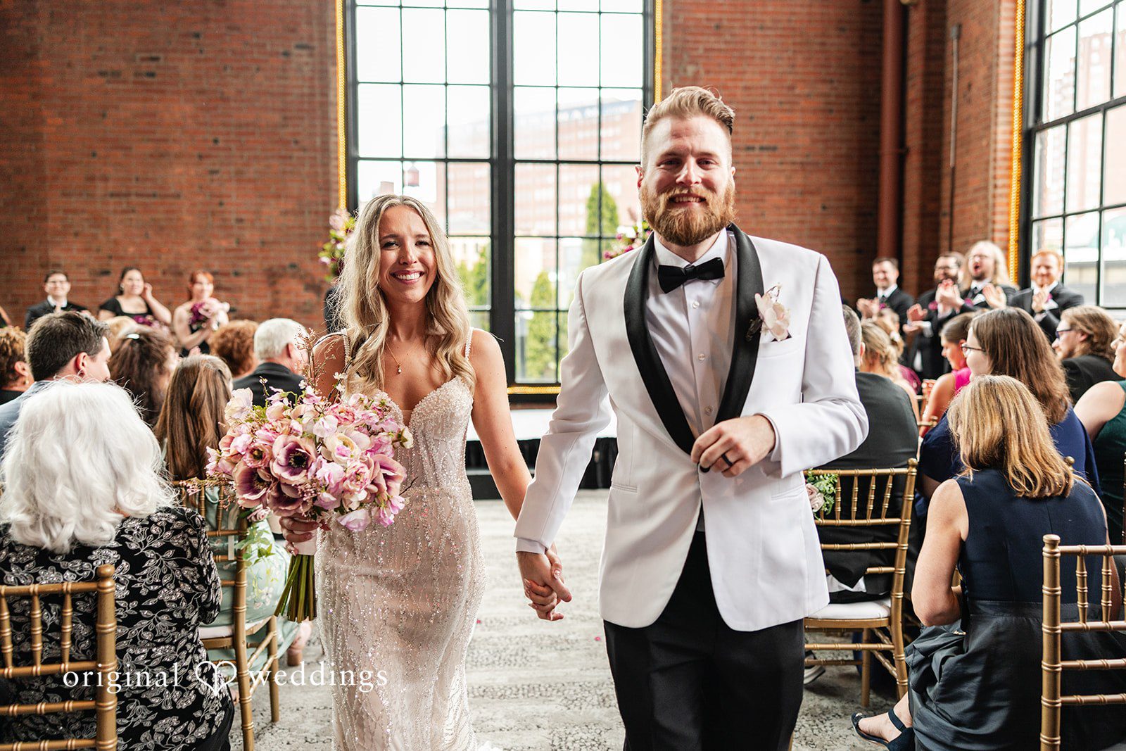 Dan + Alex A bride and groom walking happily down the reception aisle while guests applaud.