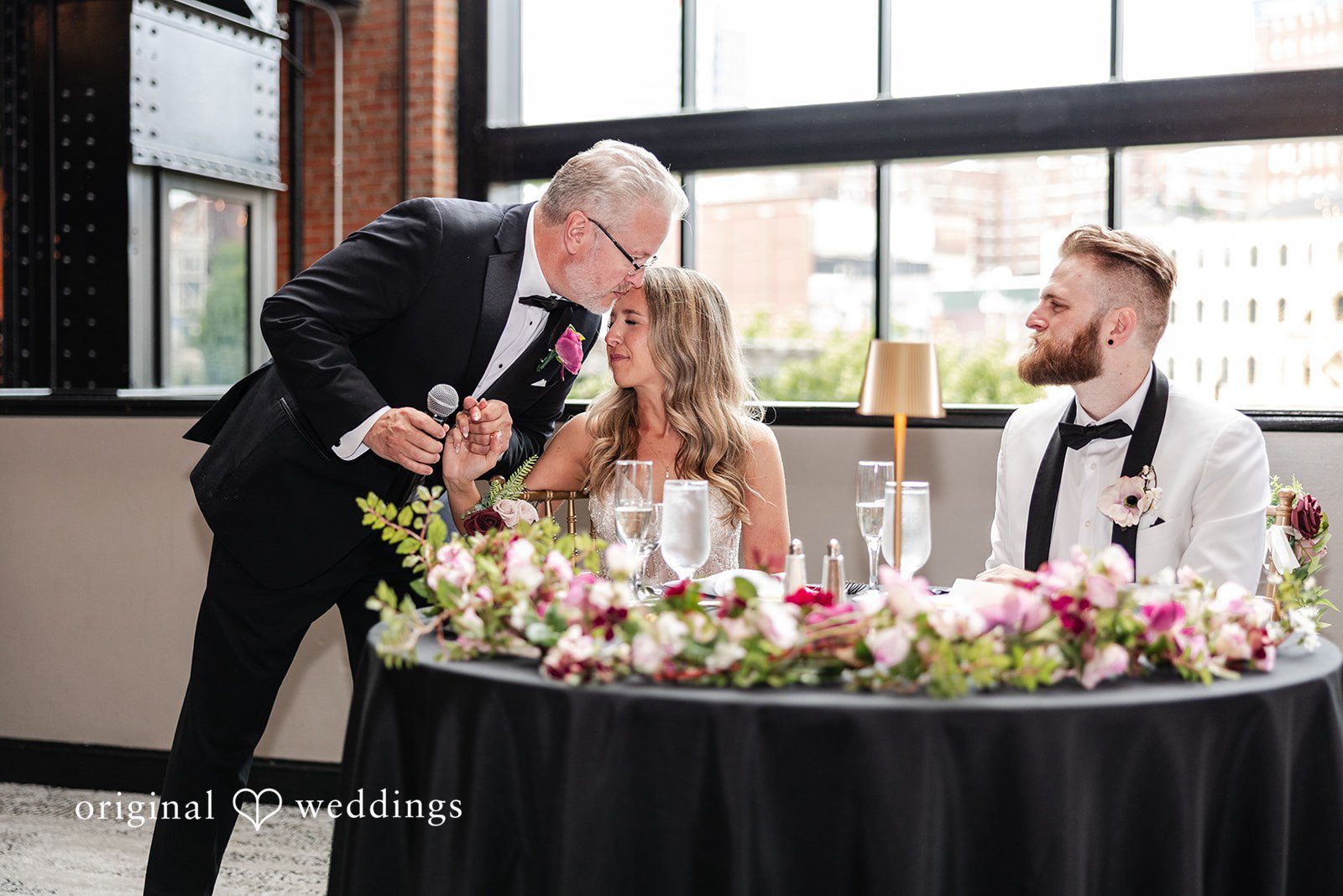 Dan + Alex A bride and groom leaning over a circular reception table decorated with flowers.