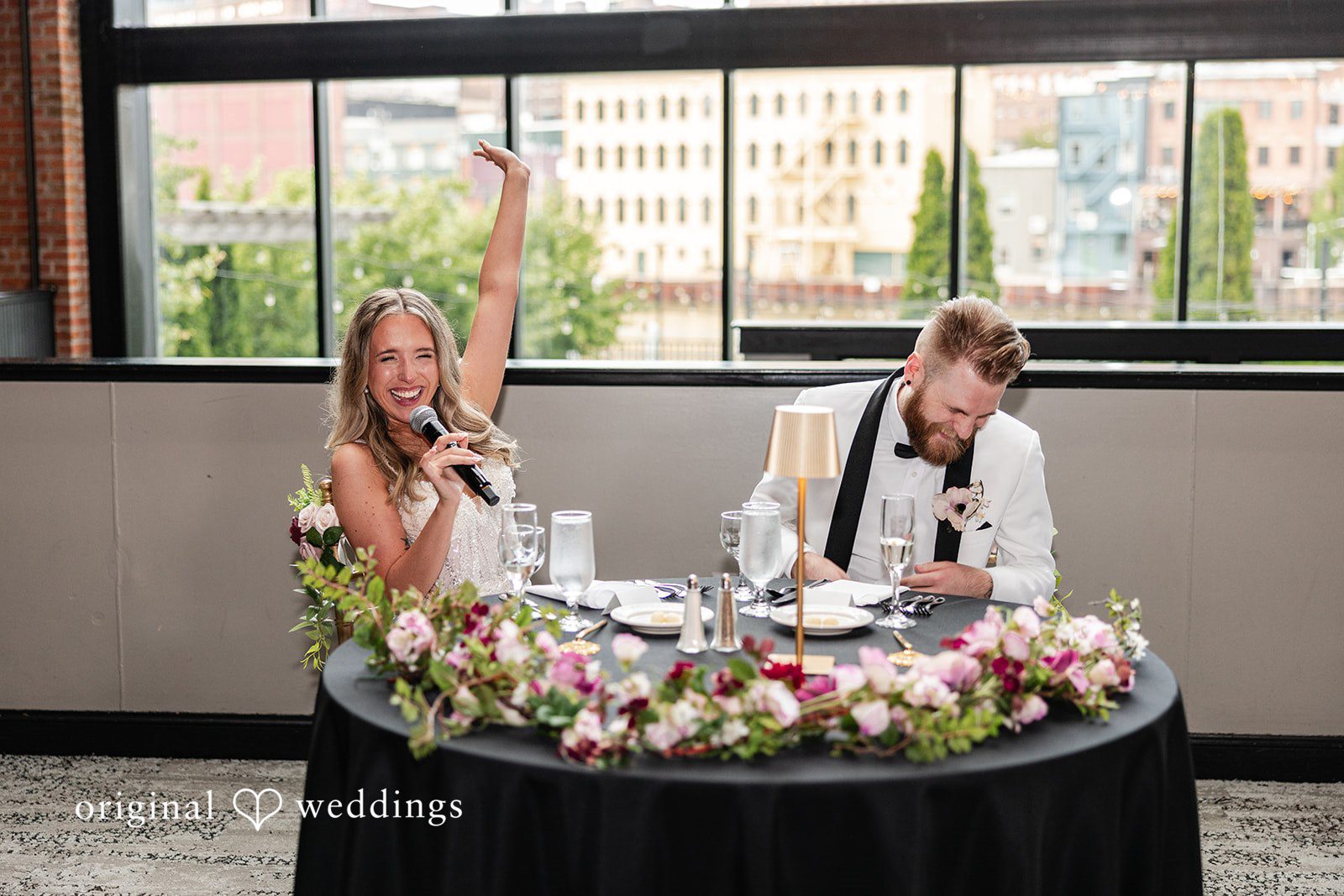 Dan + Alex A bride and groom sitting together at their decorated sweetheart table during a reception speech.