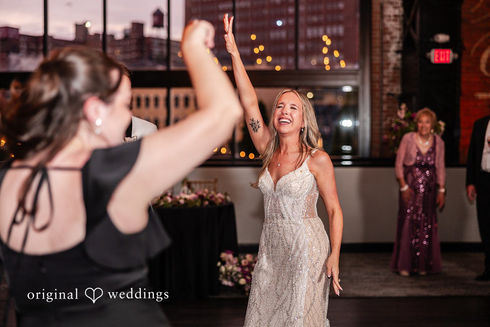 Dan + Alex A bride laughing and raising her arms while dancing with friends at the reception.