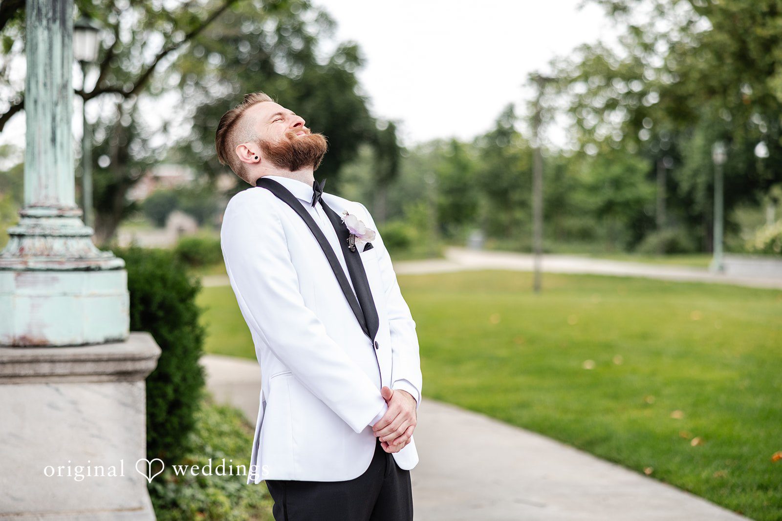 Dan + Alex A groom wearing a white tuxedo jacket with black lapels looking upward in a park setting.