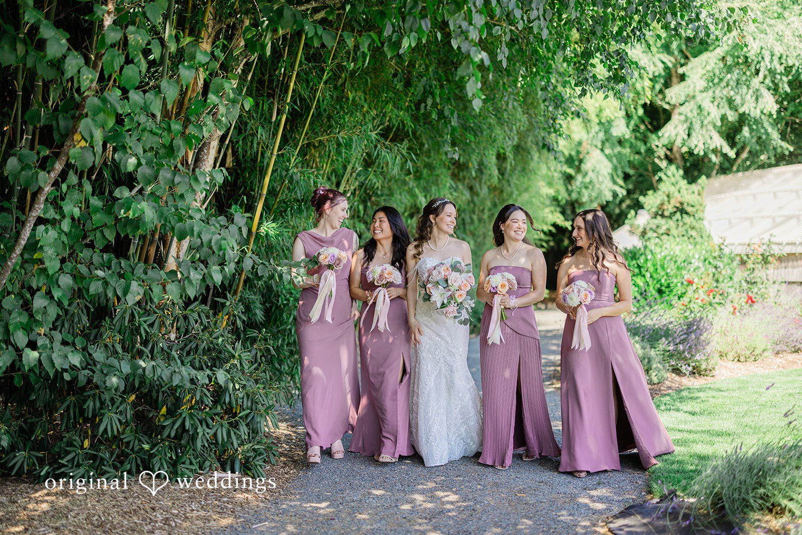 Veronica + Andrew A group of bridesmaids in matching purple dresses posing together against dense green foliage.