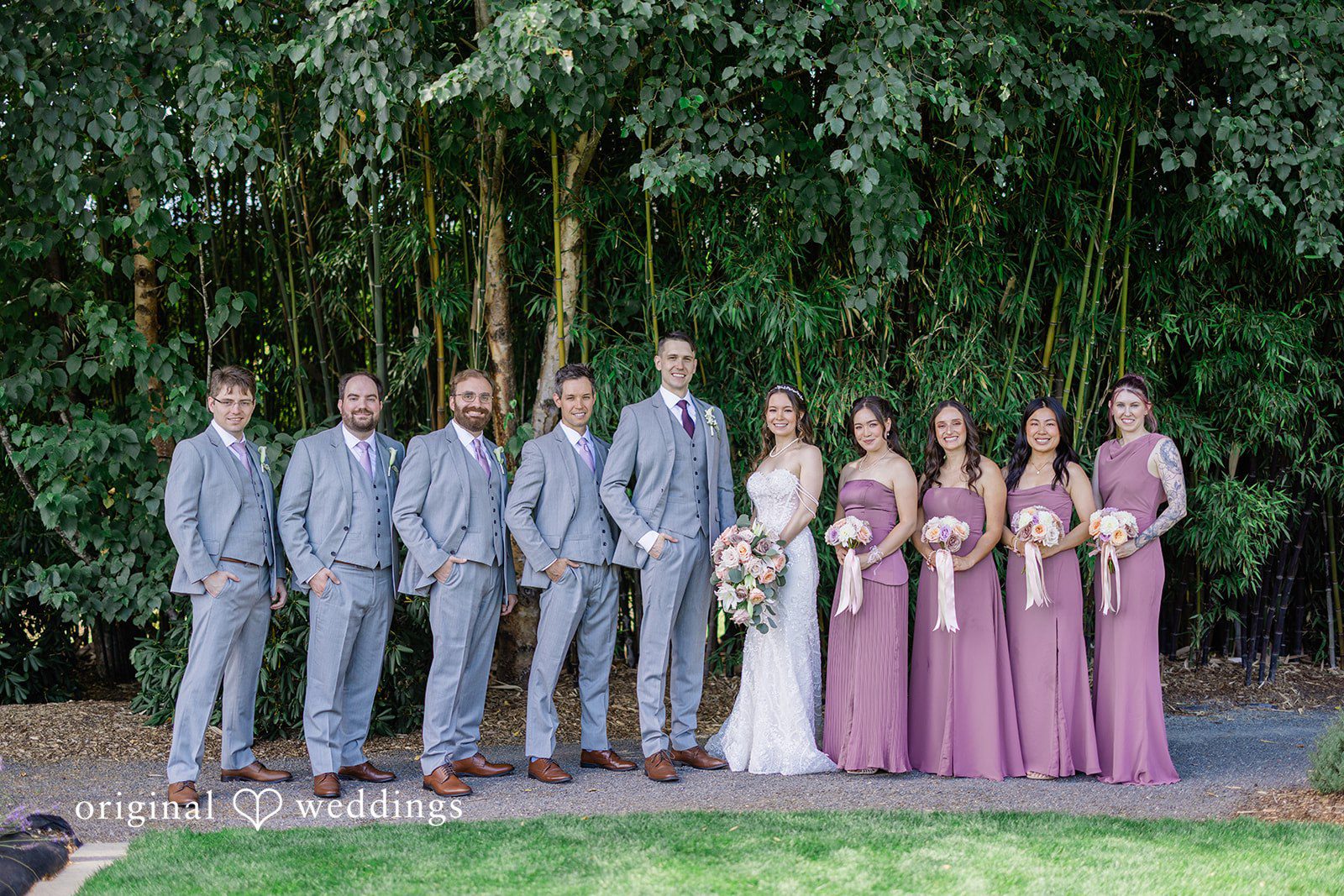 Veronica + Andrew The entire wedding party poses together in a formal line on a lawn.