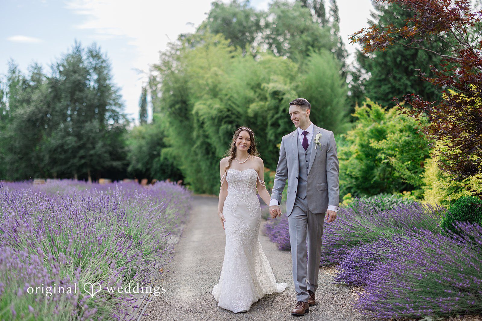 Veronica + Andrew A wedding couple walks hand-in-hand down a path running through a lavender field.