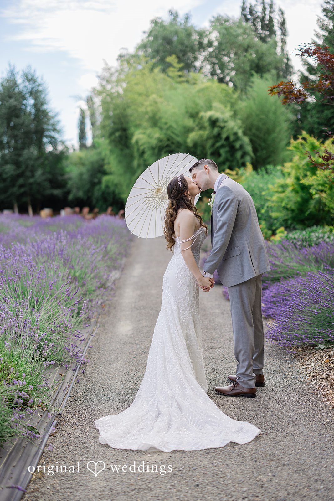 Veronica + Andrew A wedding couple kisses on a gravel path next to a lavender field.