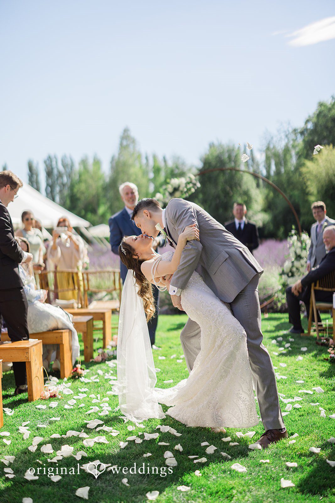 Veronica + Andrew A wedding couple sharing a joyful embrace on a sunny lawn.
