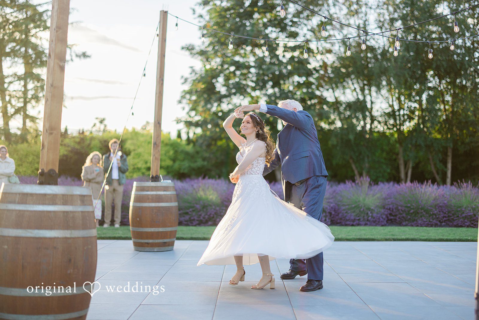 Veronica + Andrew A bride twirls in her white gown while dancing with the man near wooden barrels.