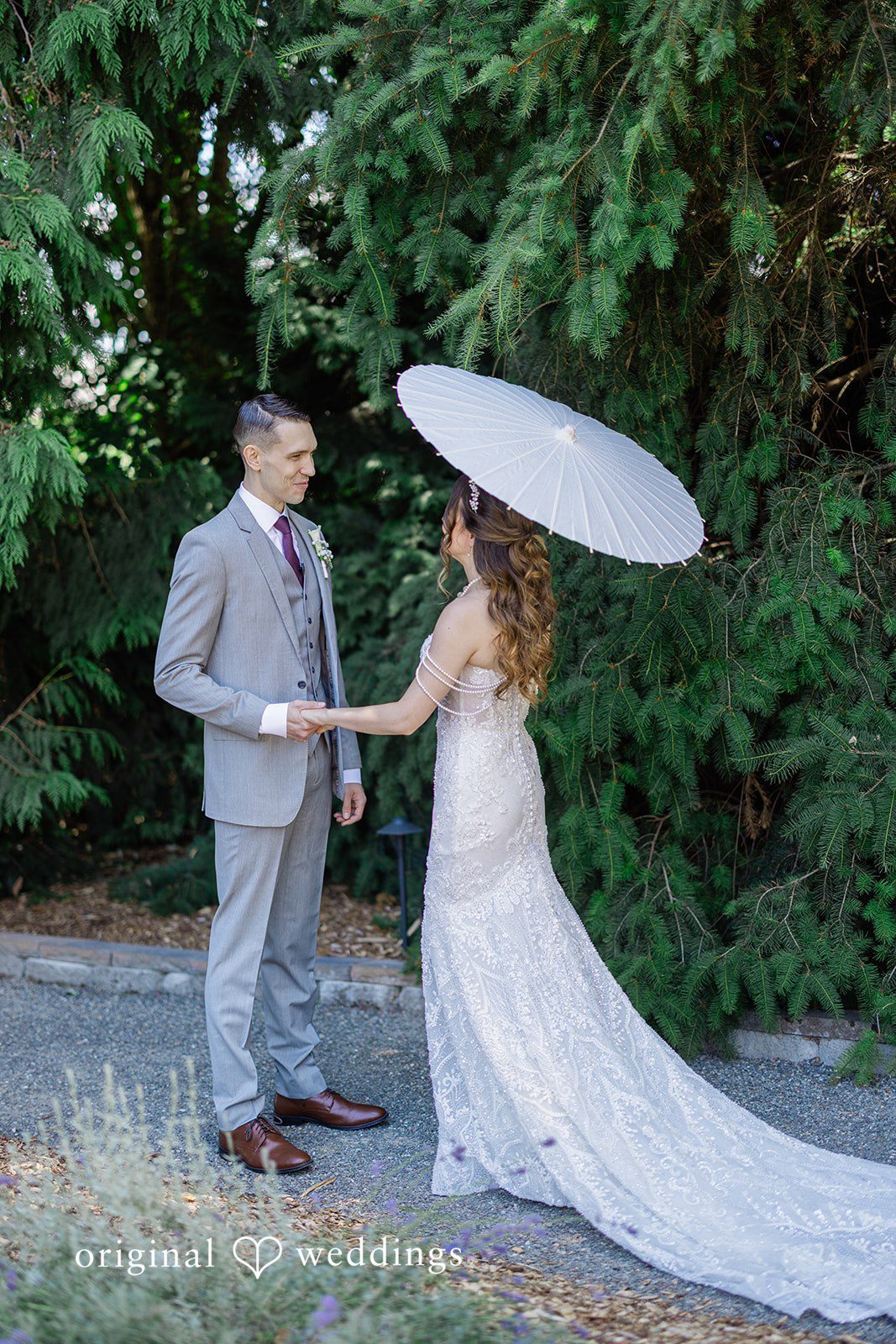 Veronica + Andrew A wedding couple stands together on a path while the bride holds a white parasol.