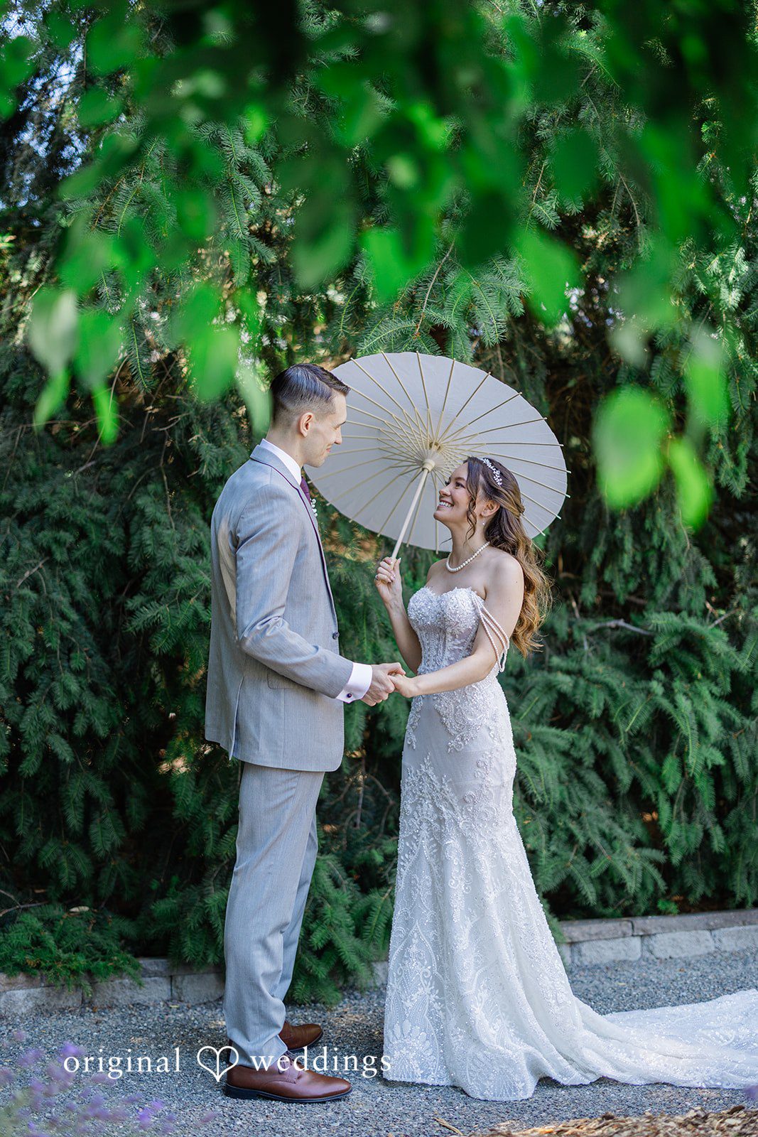 Veronica + Andrew A wedding couple holds hands and looks at each other under a white parasol.