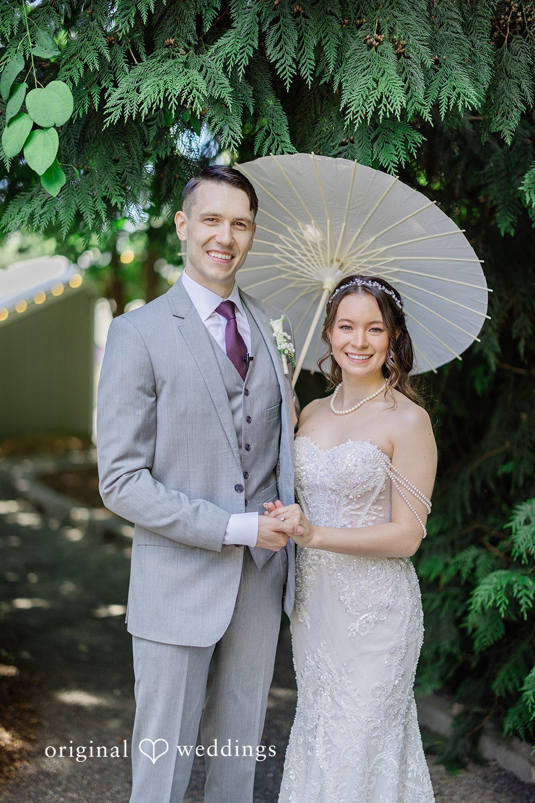 Veronica + Andrew A groom and bride stand close together while a white parasol is held above them.