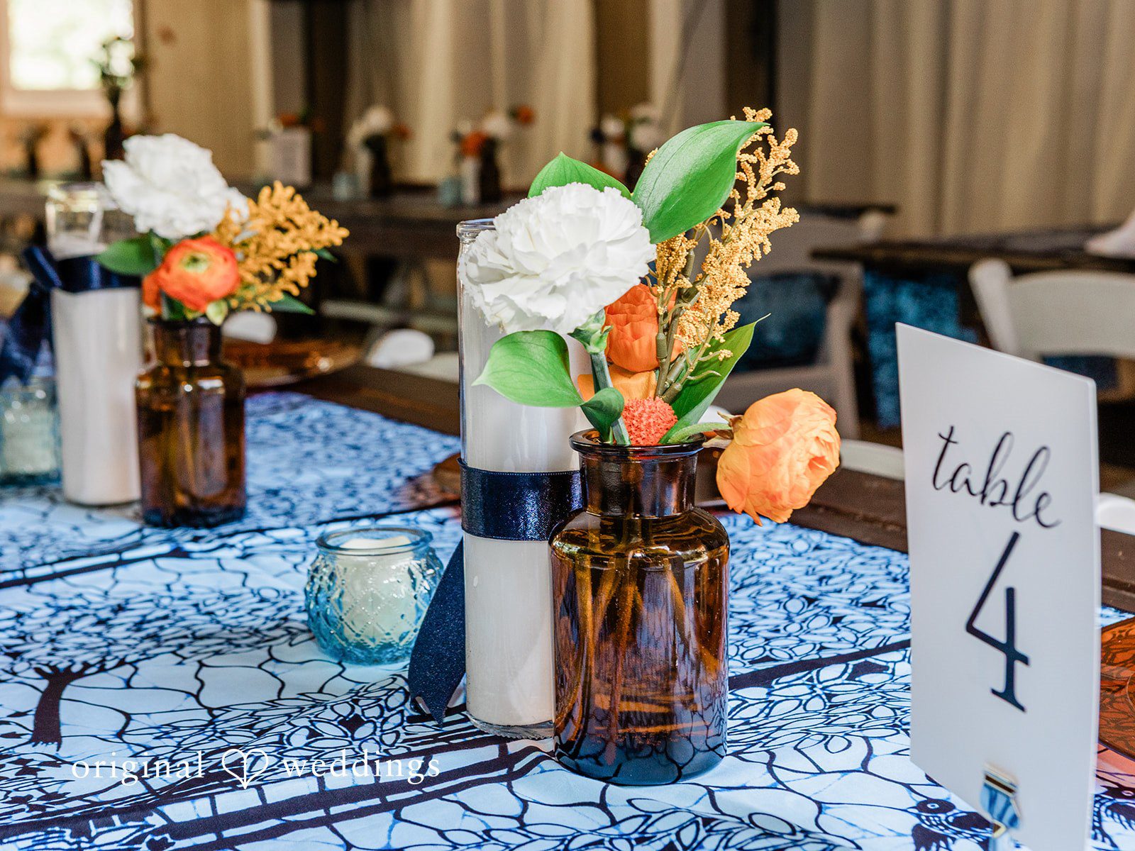 Katrina + Japhet Close-up of a wedding table setting with a patterned blue runner and a clear table number four sign.