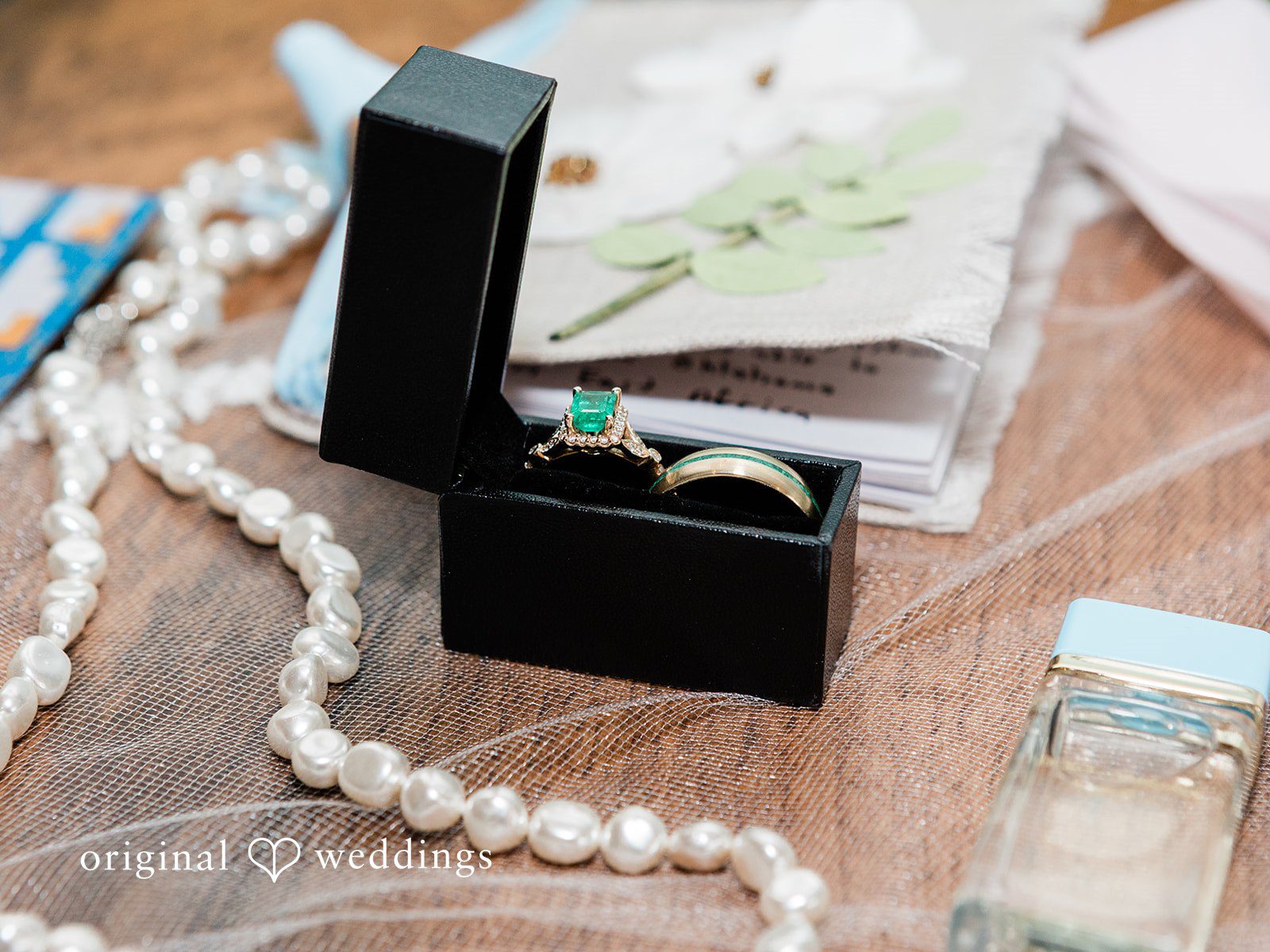 Katrina + Japhet Flat lay arrangement of a wedding ring box, pearl necklace, and stationery details.